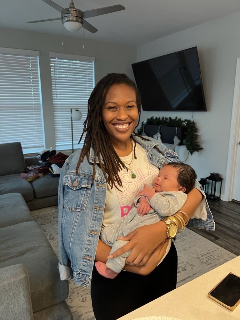 A woman in a denim jacket holding a baby in a modern living room.