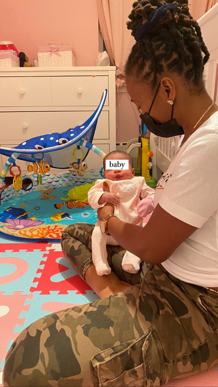 A person holding a baby in a playroom with colorful play mat and activity gym.