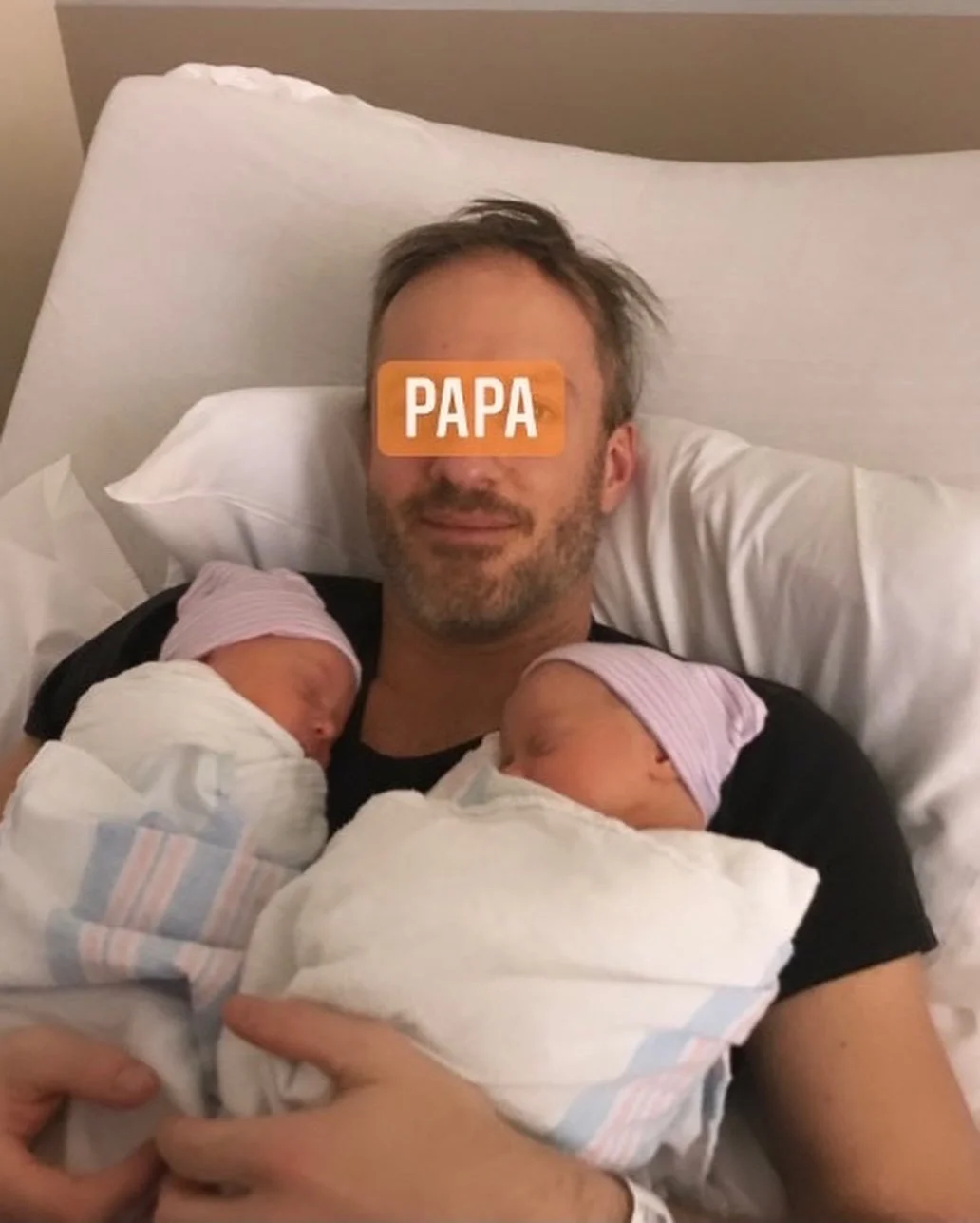A person labeled 'Papa' holding two newborn babies wrapped in hospital blankets, both wearing knitted caps, lying on a hospital bed.