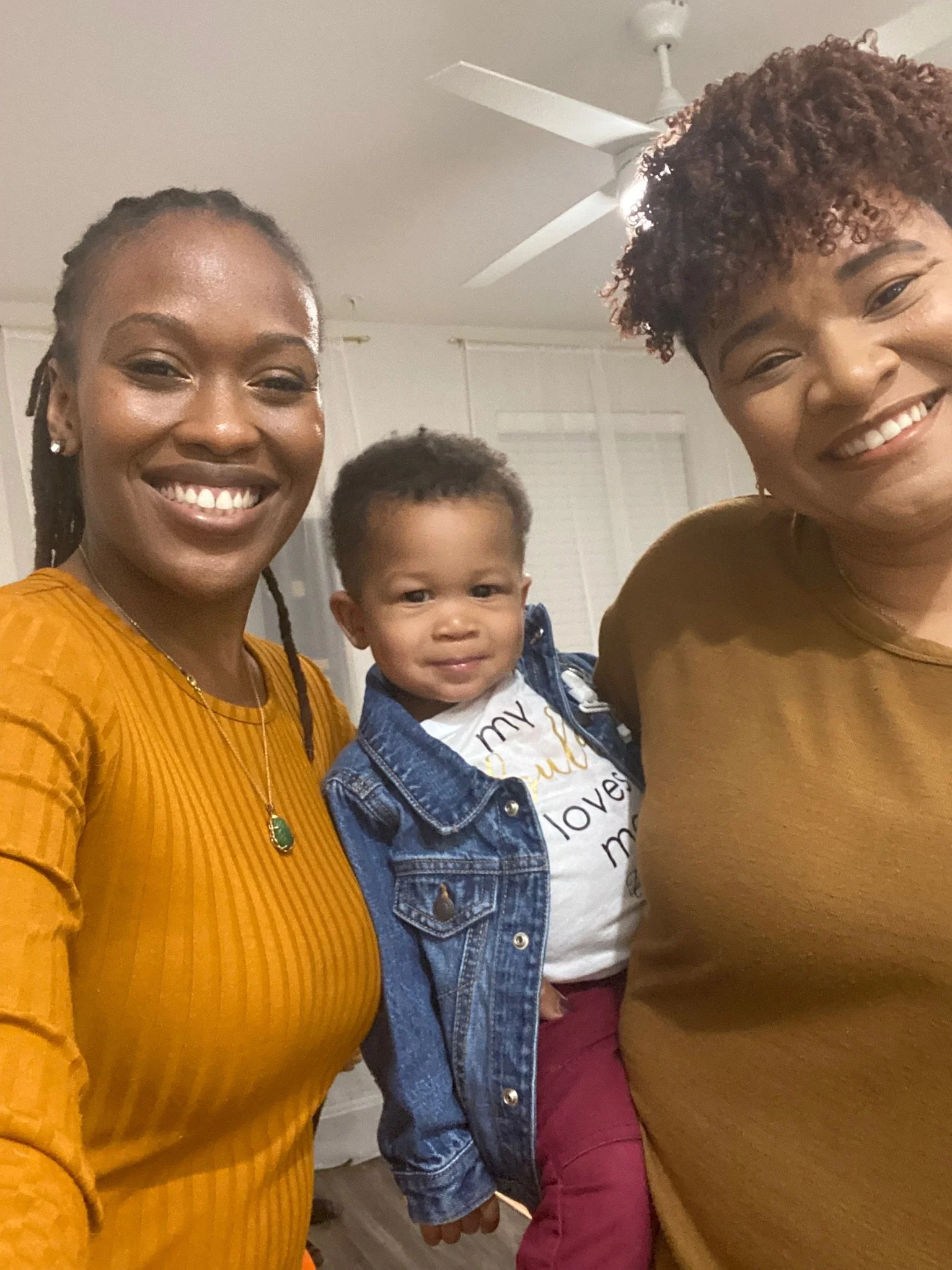 Two adults and a child smiling indoors, wearing casual clothing.