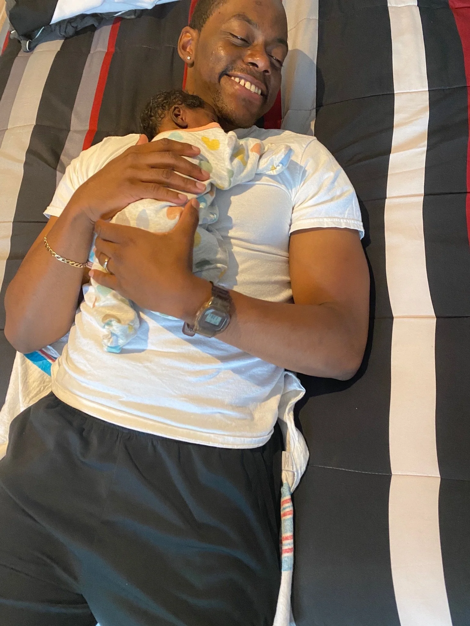 A man lying on a bed holding a sleeping baby on his chest, both appear content and relaxed.
