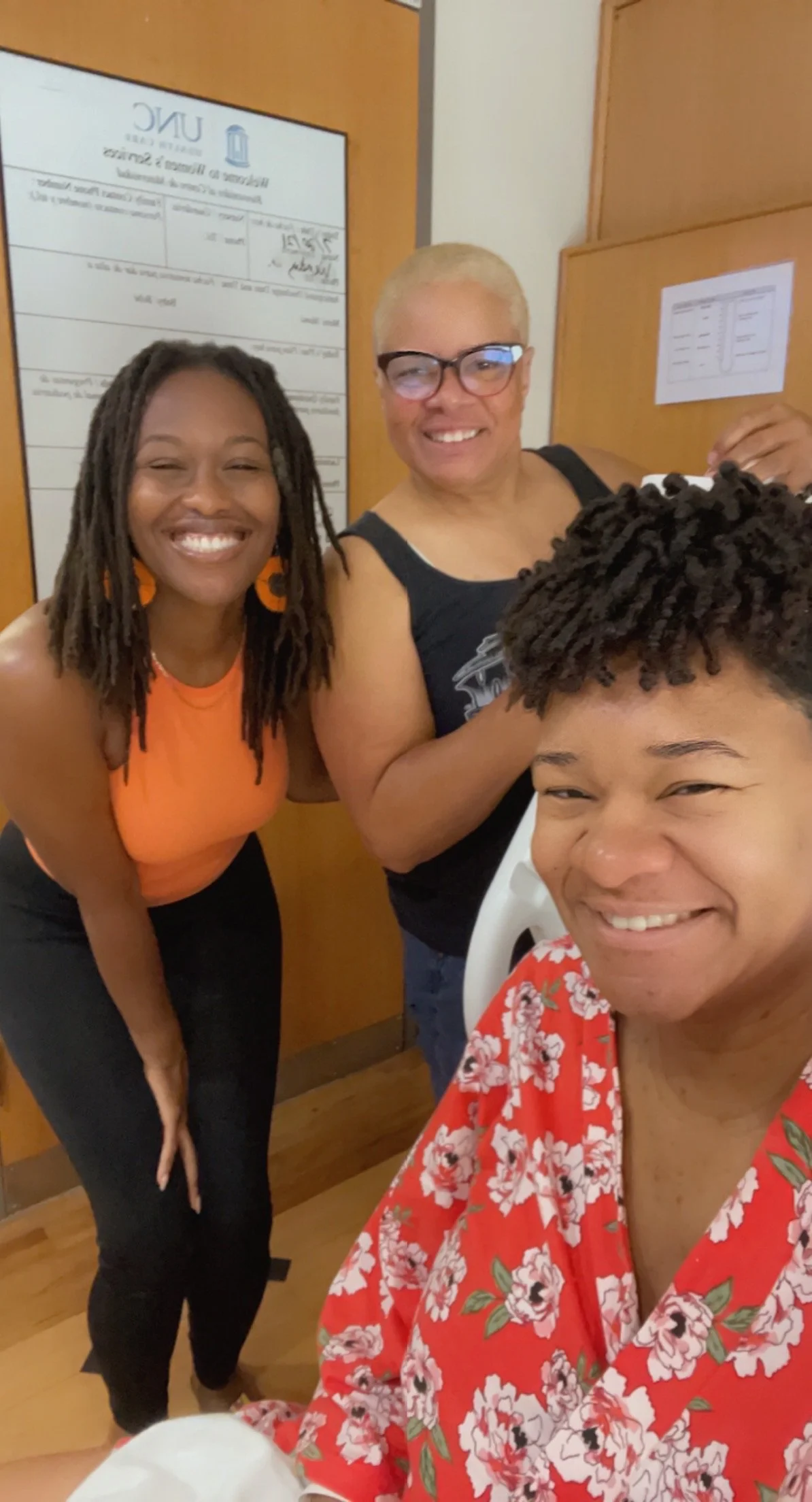 Three people smiling indoors in front of a UNC Family Medicine sign.
