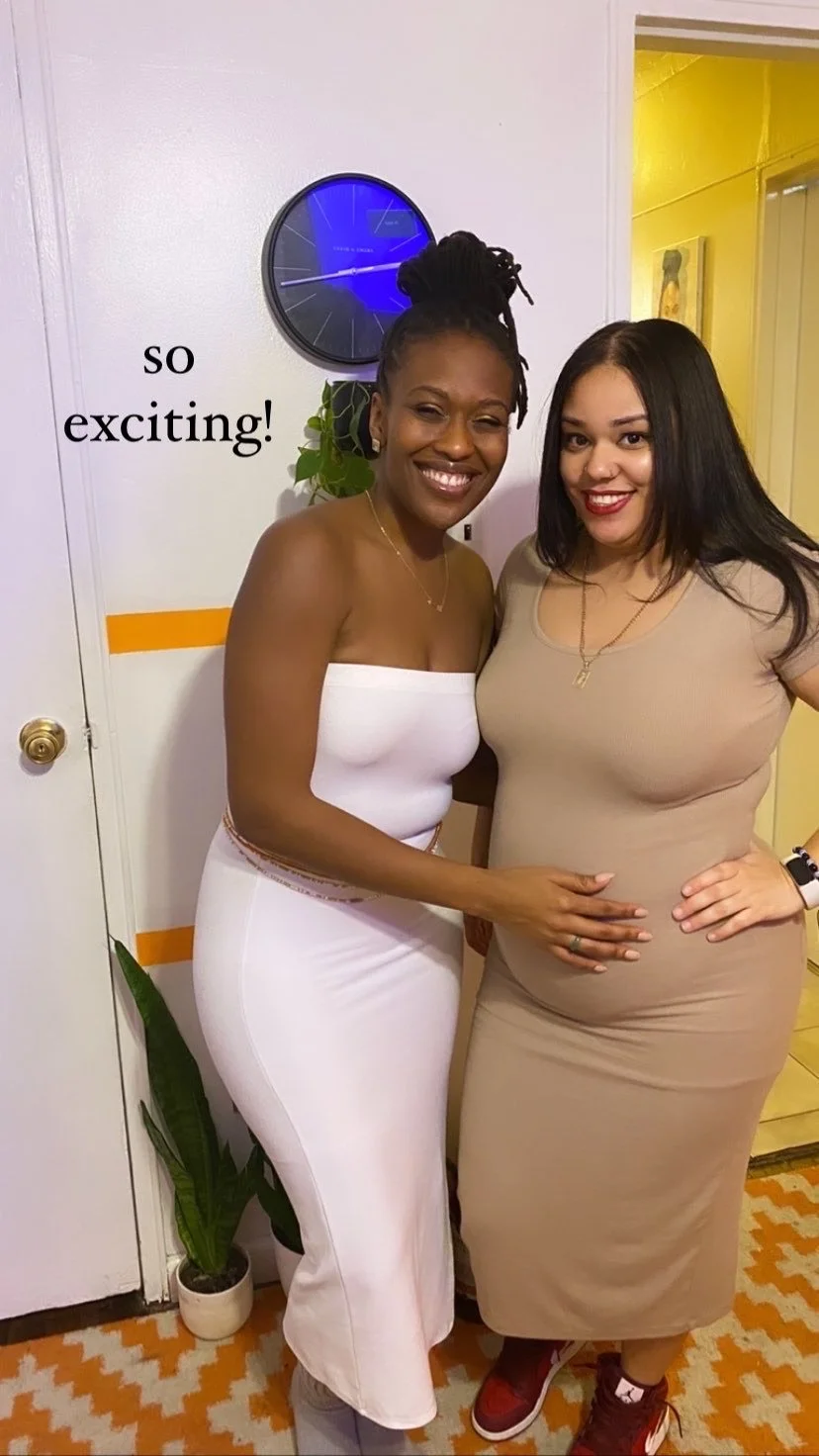 Two women smiling indoors, one with hand on the other's pregnant belly, standing near a wall with a blue clock and a plant. Text "so exciting!" is visible.