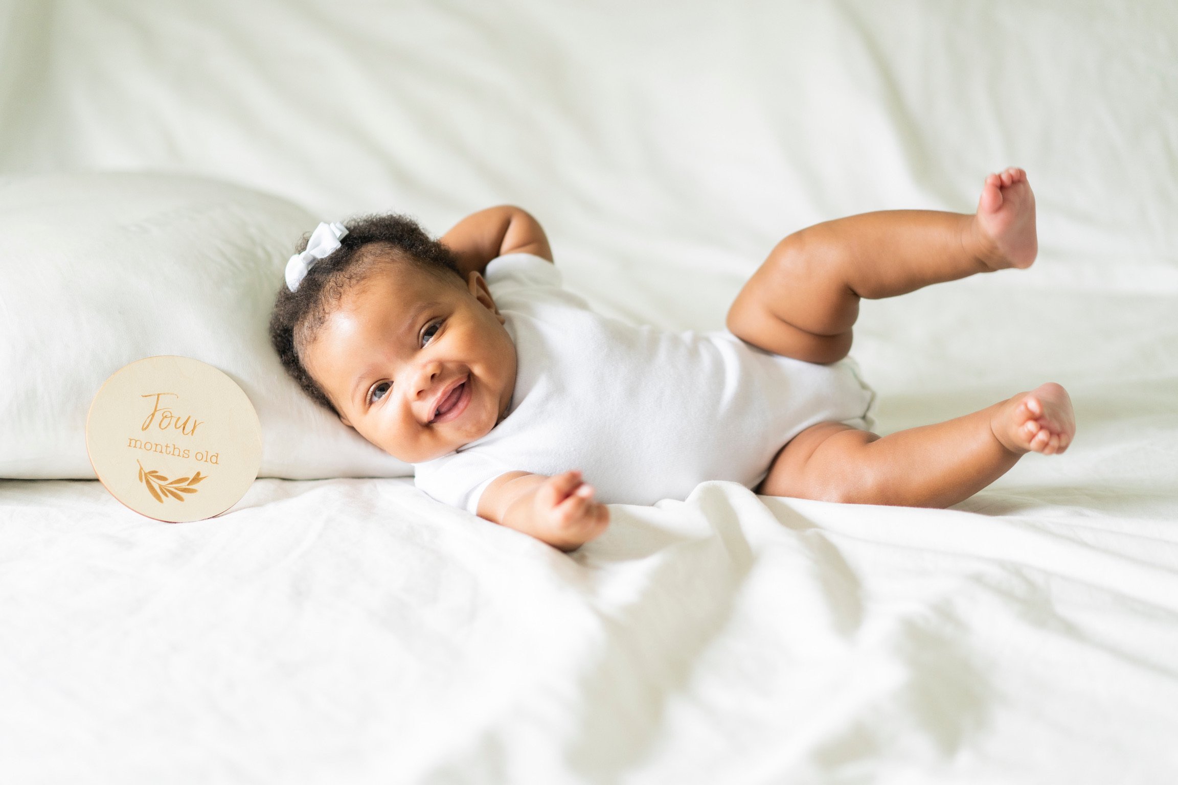 Smiling baby lying on white blanket next to "Four months old" sign.