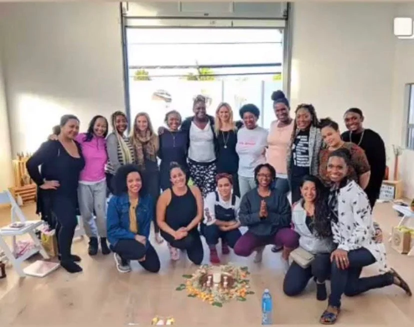Group of people gathered indoors, smiling, with candles and decor on floor in center.