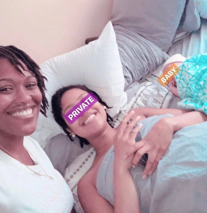 Three people in a room, two adults and one baby, lying on a bed. The adults are smiling, and the baby's face is partially covered with a blanket. Text labels cover the faces of the adults and baby.