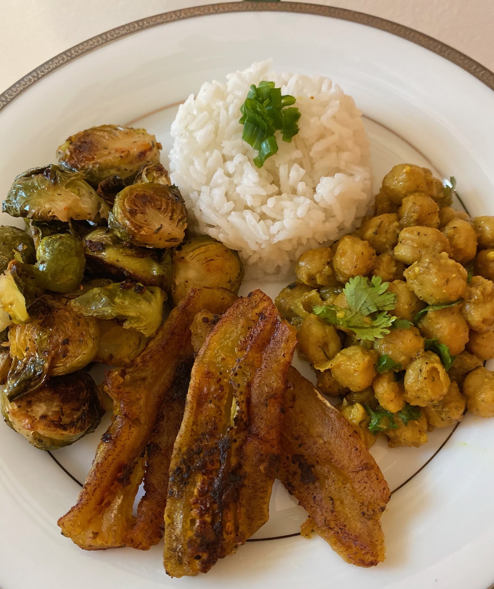 Plate with rice, roasted Brussels sprouts, chickpea curry, and fried plantains.