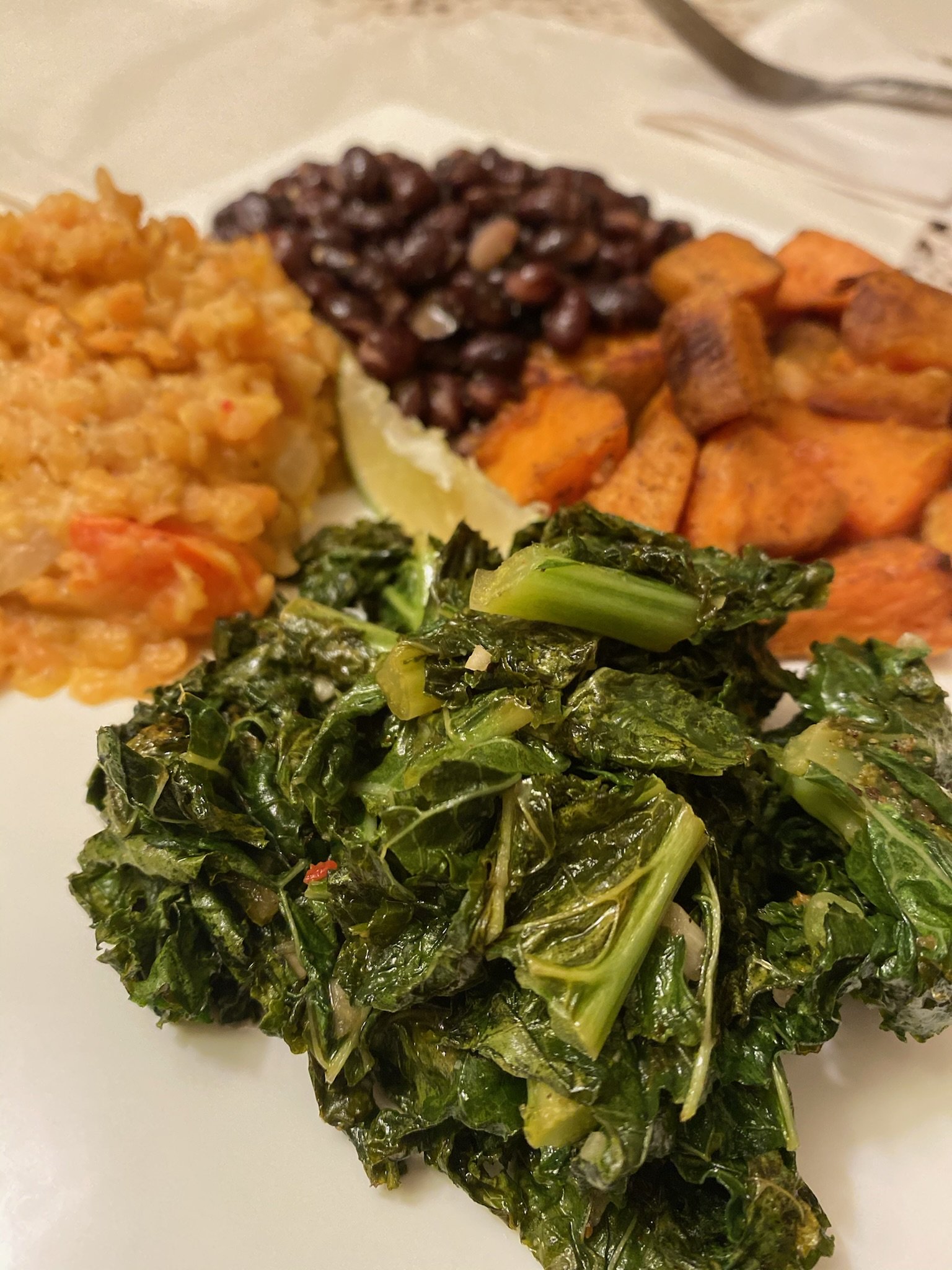 Plate with cooked kale, roasted sweet potatoes, black beans, and mashed lentils.