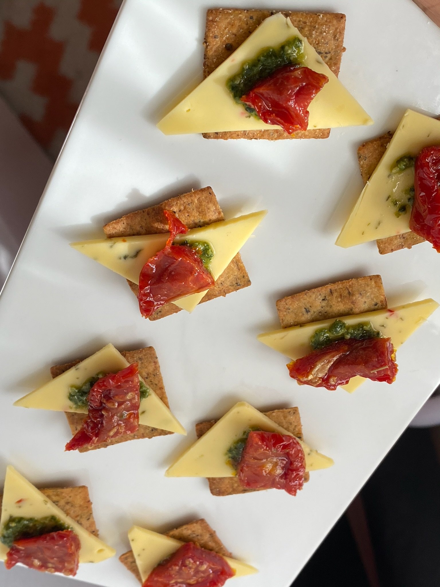 Crackers topped with cheese, pesto, and sun-dried tomatoes on a serving plate.