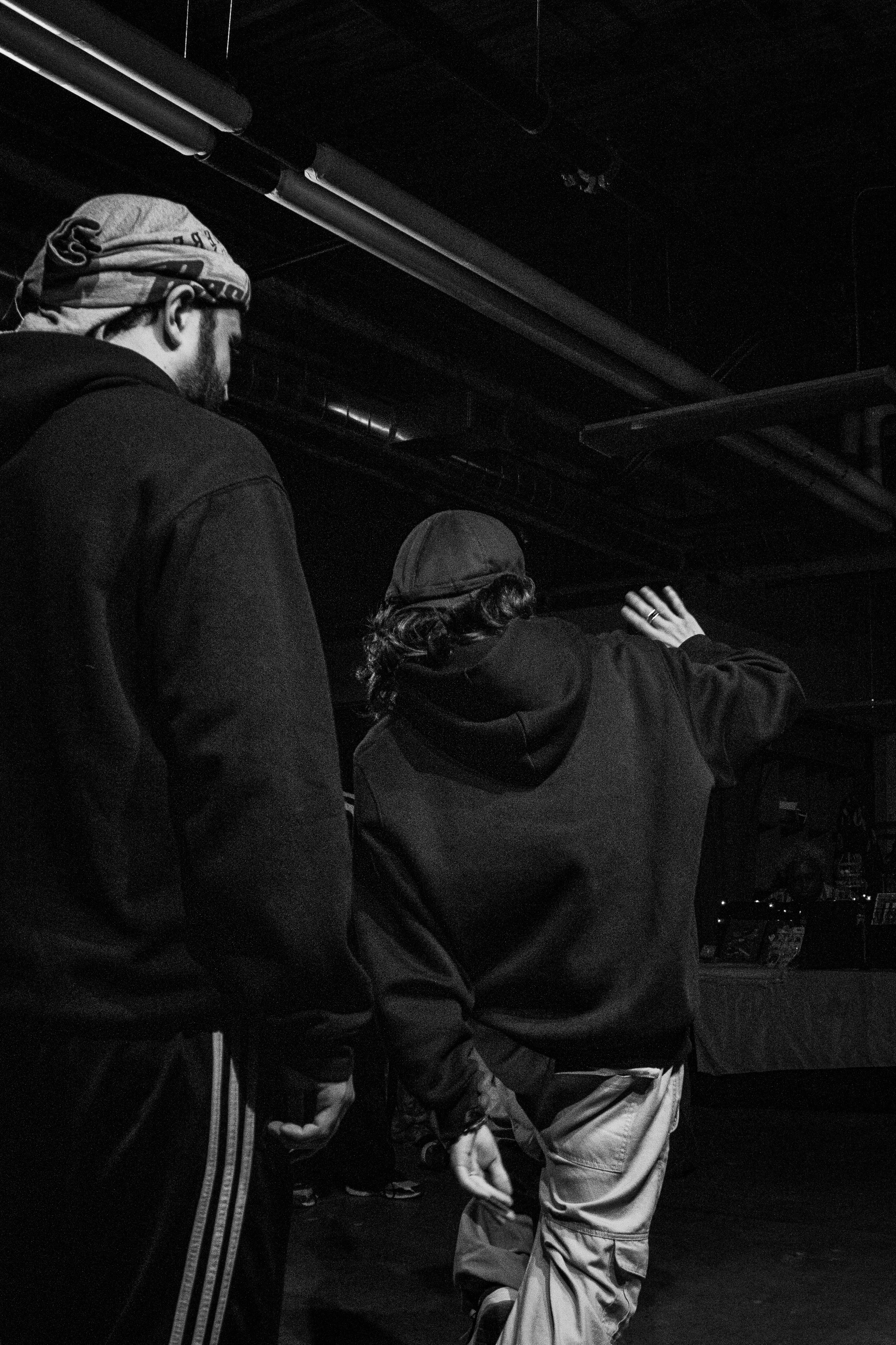 Three people stand in a dark indoor space, one person appears to be explaining or demonstrating something to the other two, with a focus on the person's hand gesture.
