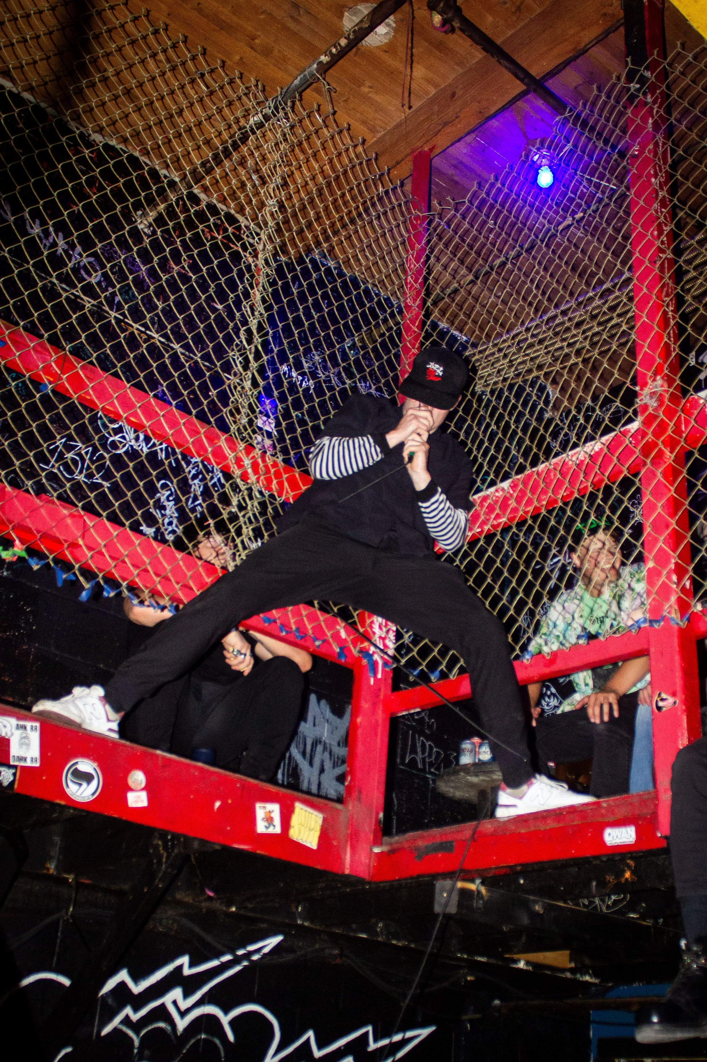 People sitting and standing on a red structure in a bar or nightclub, with a wooden ceiling and blackboard behind them.