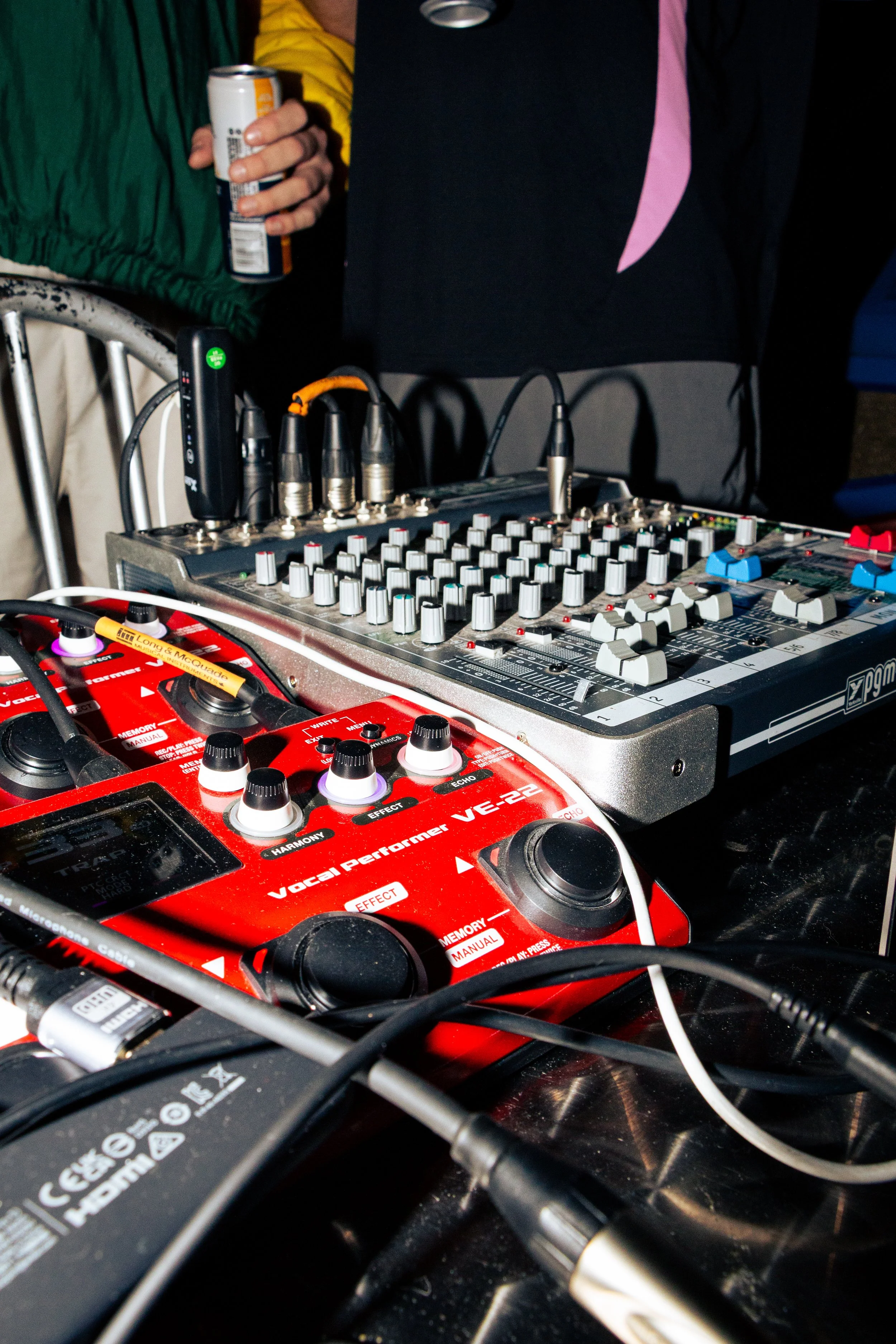 Close-up of audio equipment including a red Vatal Performer VE-22 pedal, a mixer, and various connected cables, with a person's hand holding a can of drink in the background.