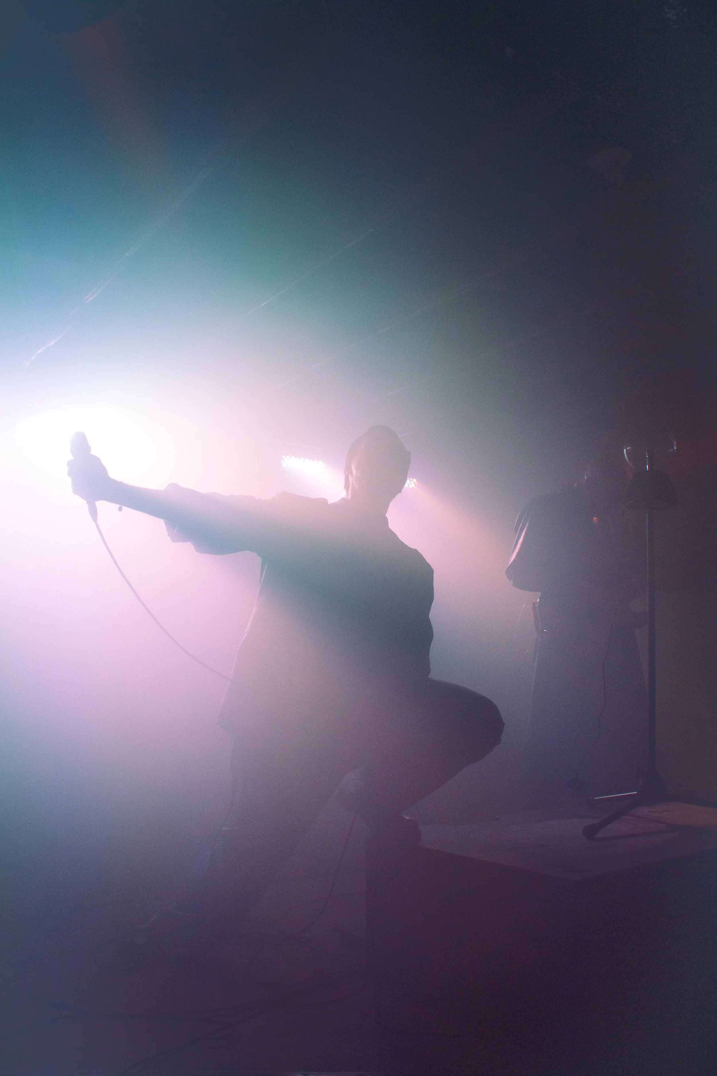Silhouettes of two people on a stage or in a dark room with colorful stage lights creating a smoky atmosphere.