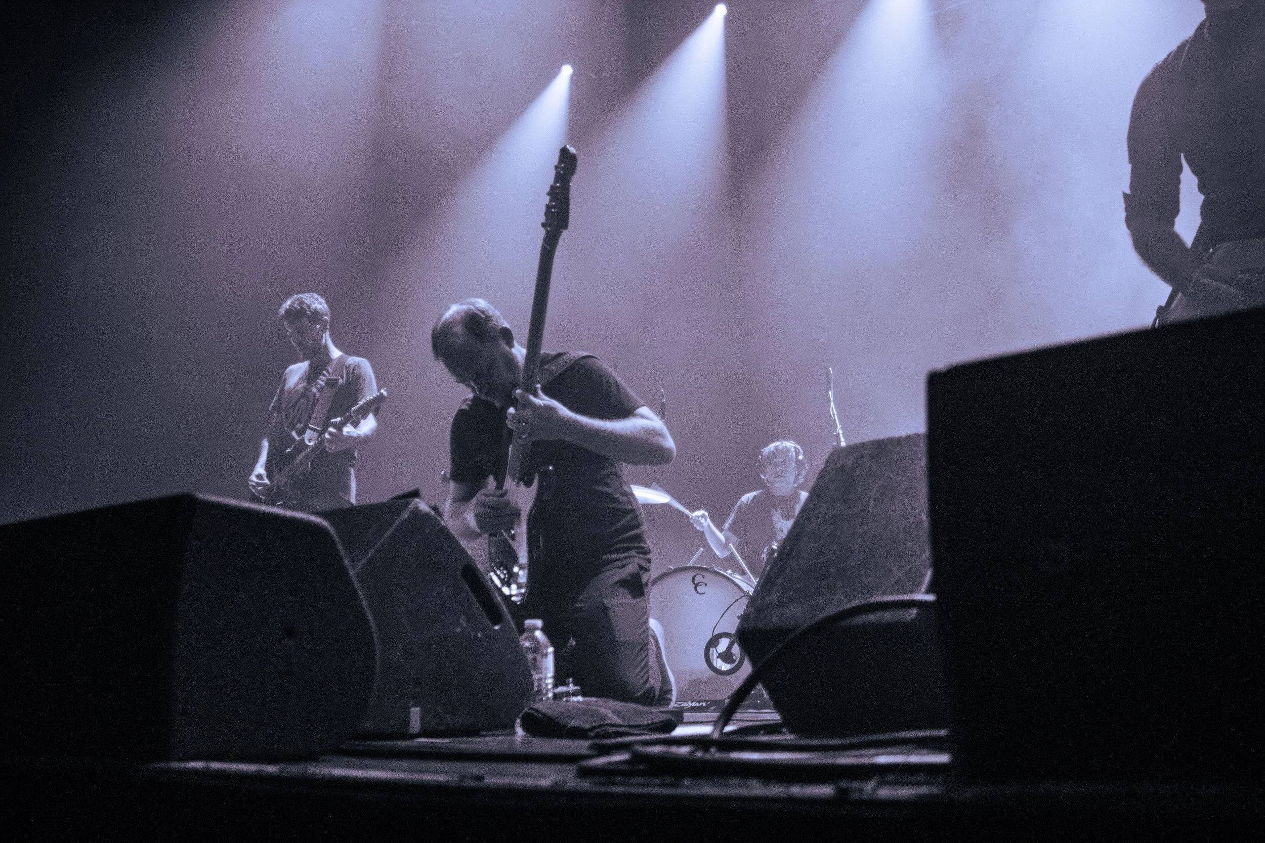 A band performing on stage with musicians playing guitars and drums, illuminated by stage lights.