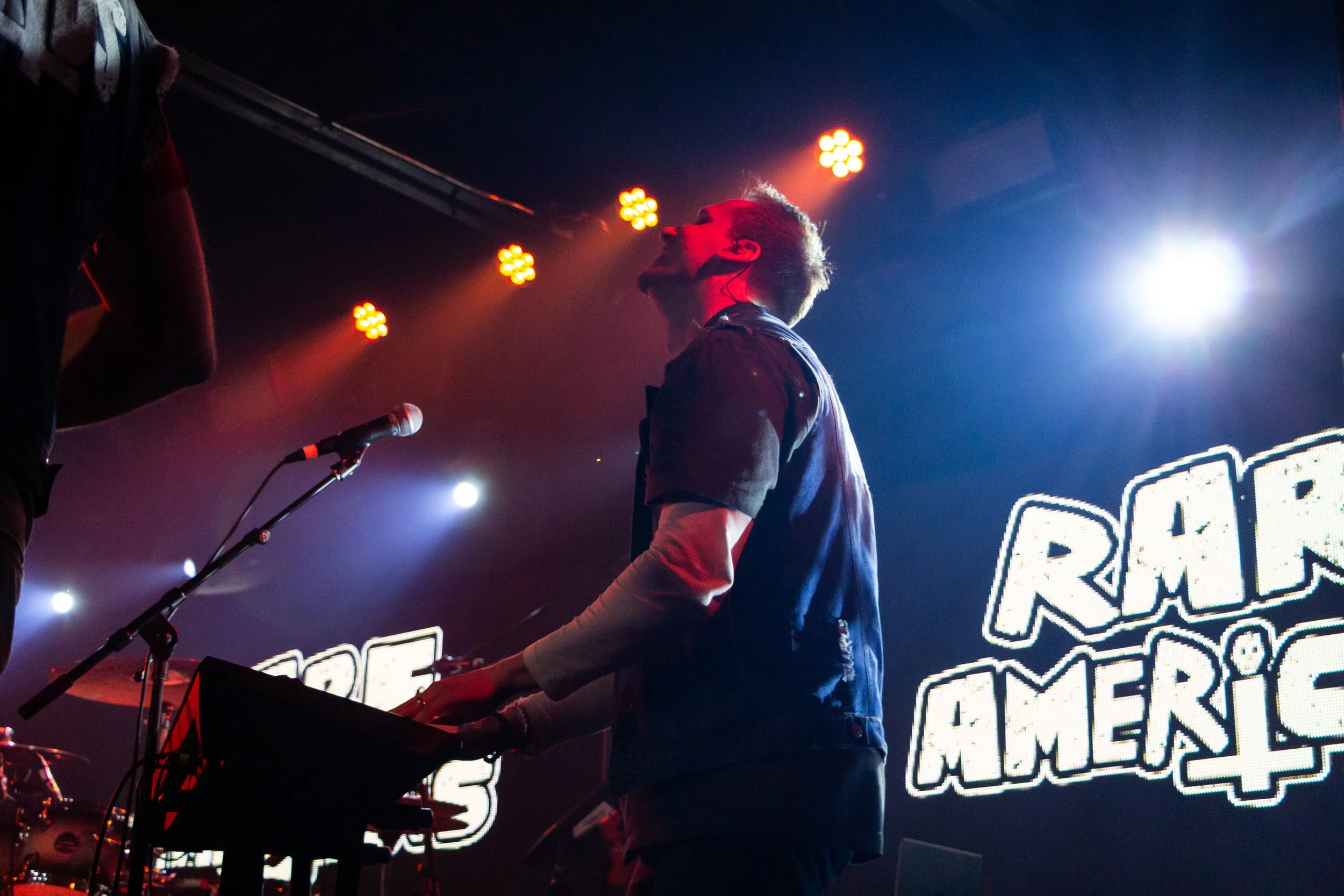 A musician playing the keyboard on stage with colorful lights and decorative signage in the background.