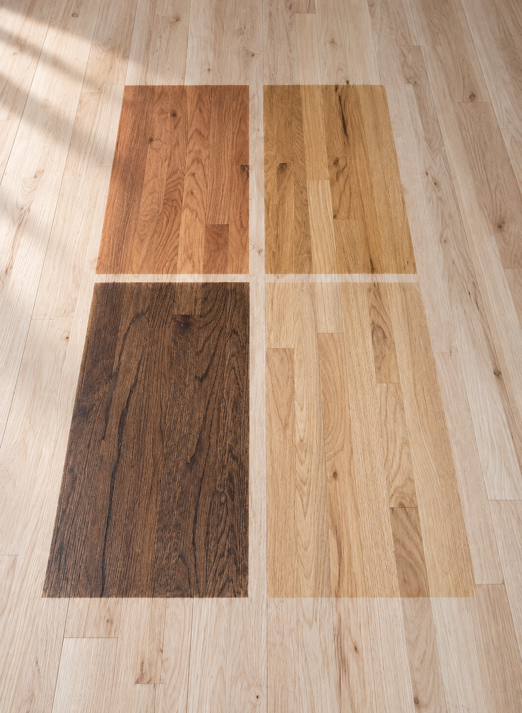Color swatches of different shades of hardwood flooring laid on a wooden floor.