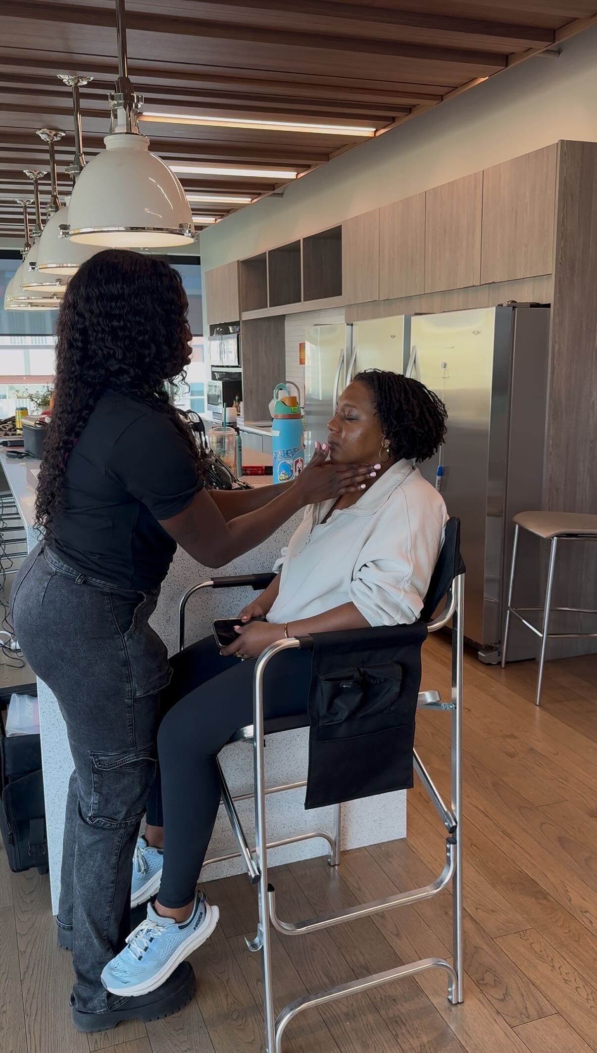 Makeup artist Ness applying glam to a seated woman inside the CMA office, showcasing her deep-skin expertise and professional event makeup work during CMA Awards preparations.