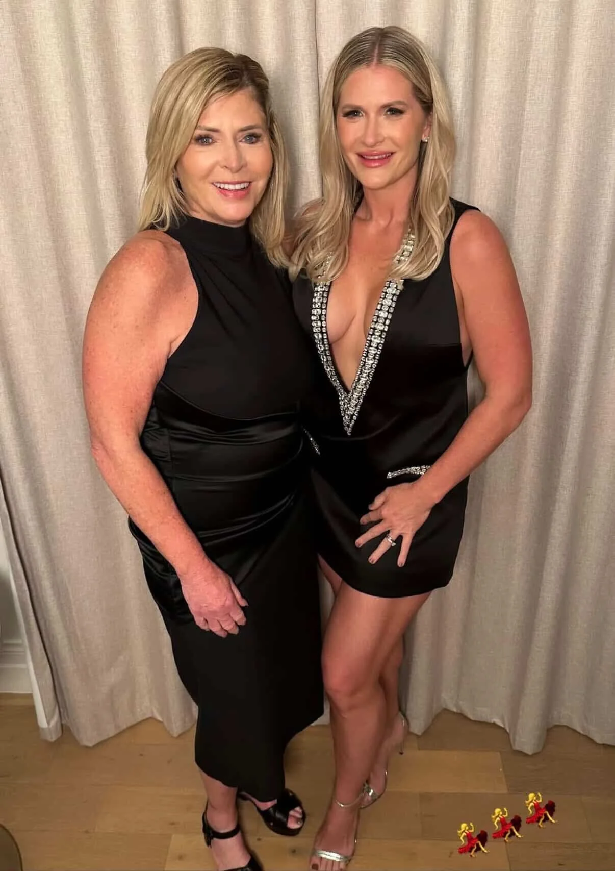 Two women with soft polished waves, radiant complexions, defined eyes, and neutral glam lips posing together in black dresses before attending the CMA Awards.
