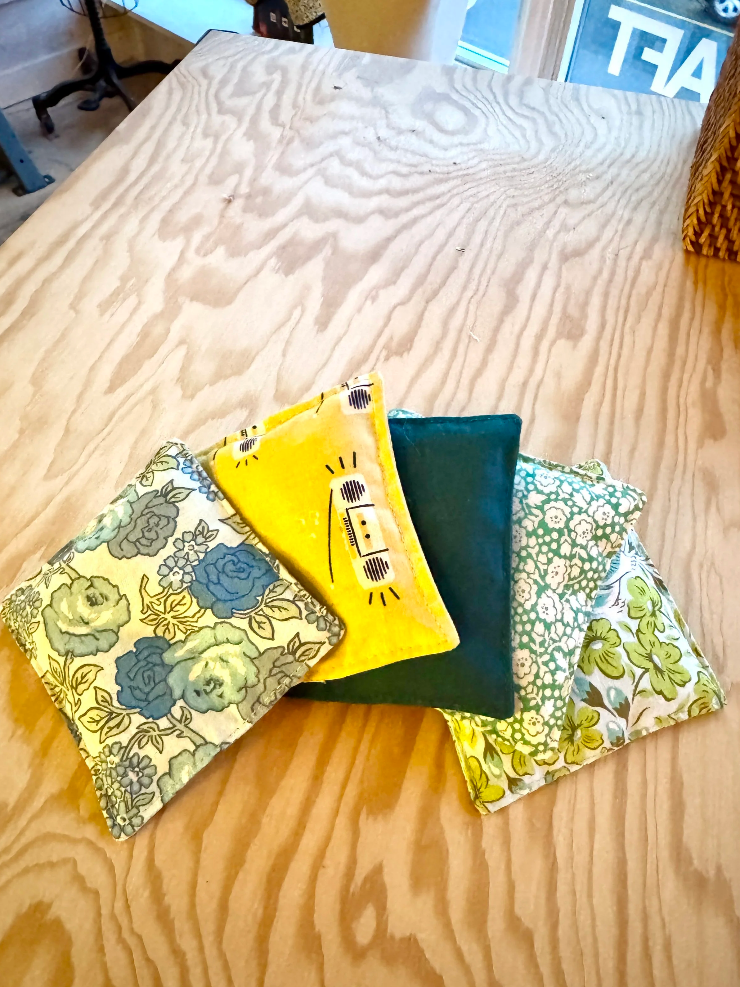 A pile of six fabric napkins in various colors and patterns on a wooden table with a light wood grain finish.