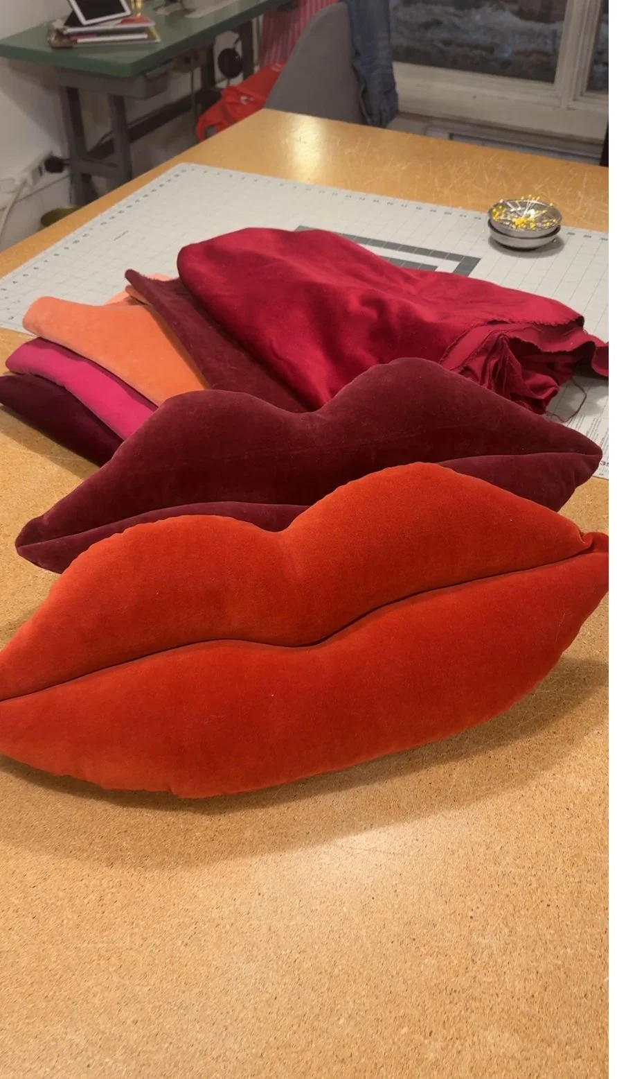 Colorful velvet pillows shaped like lips placed on a wooden table.
