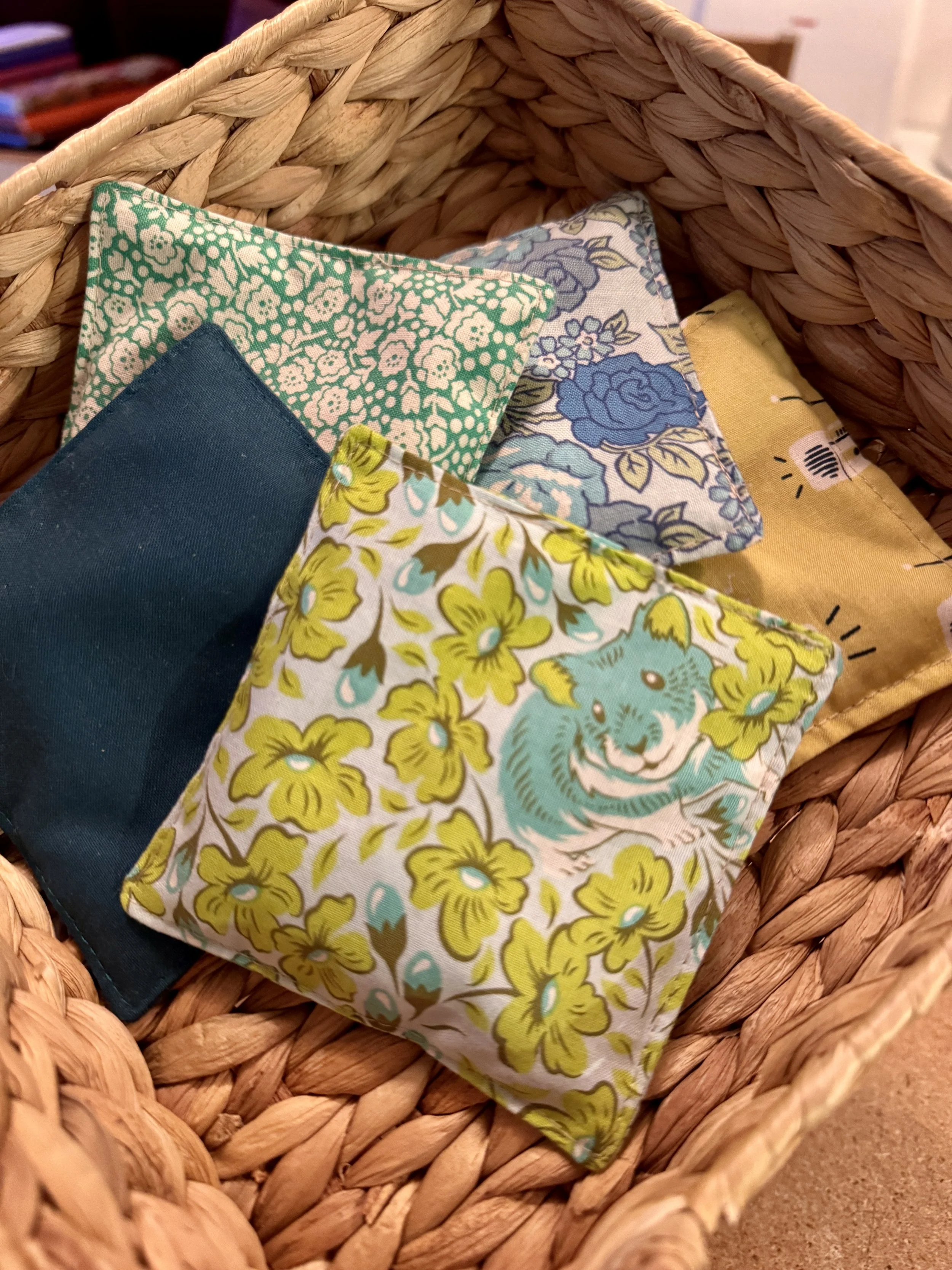 A woven basket containing five cloth napkins with various floral and animal patterns.