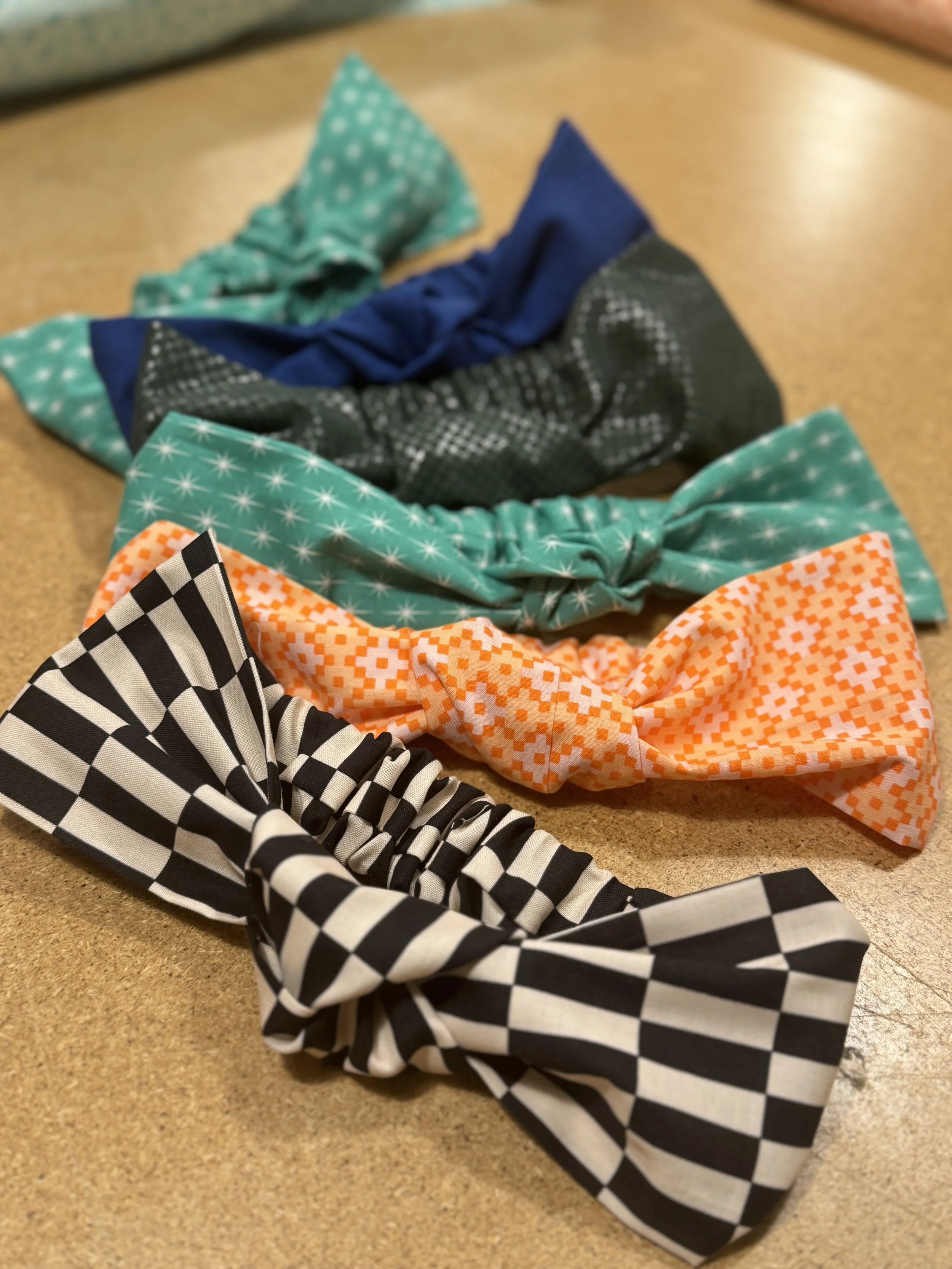 Headbands that students made in the Learn to Sew 1 class. The headbands are a knotted style, with a large knot that sits at the top of the head. The headbands are splayed out artistically. They are made of colorful quilting cotton including tula pink