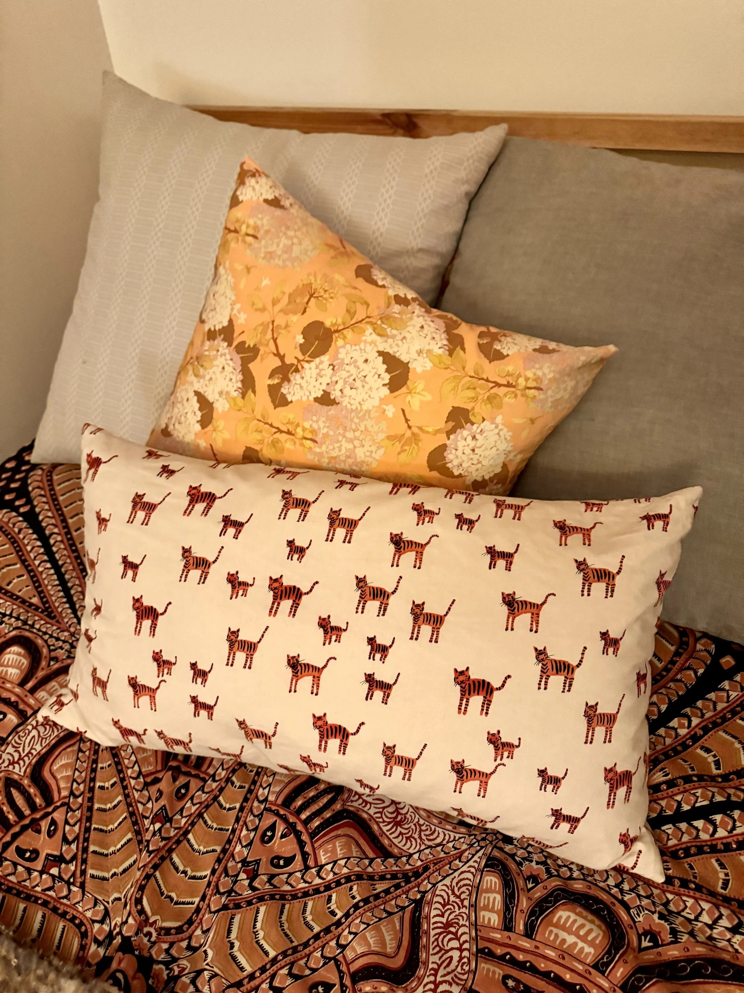 Arrangement of four pillows on a bed with a patterned blanket. The pillows include one with a floral print, one plain gray, and one with a zebra print pattern.