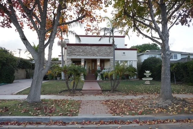 Residential house with a lawn, trees, and a sidewalk in front.