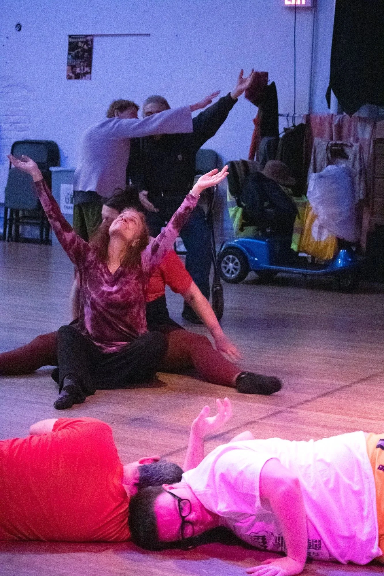 A picture of a group of people dancing. Two stand, two sit, and two lie on the floor. A mobility scooter is seen in the background.