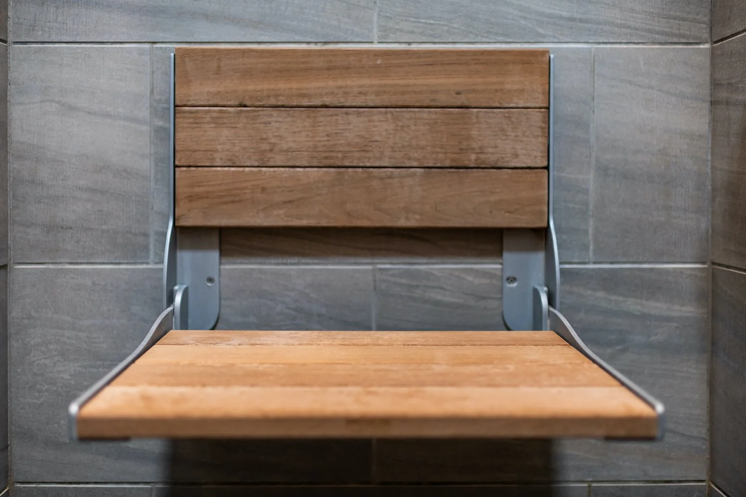 Empty wooden bench with metal frame against tiled wall.