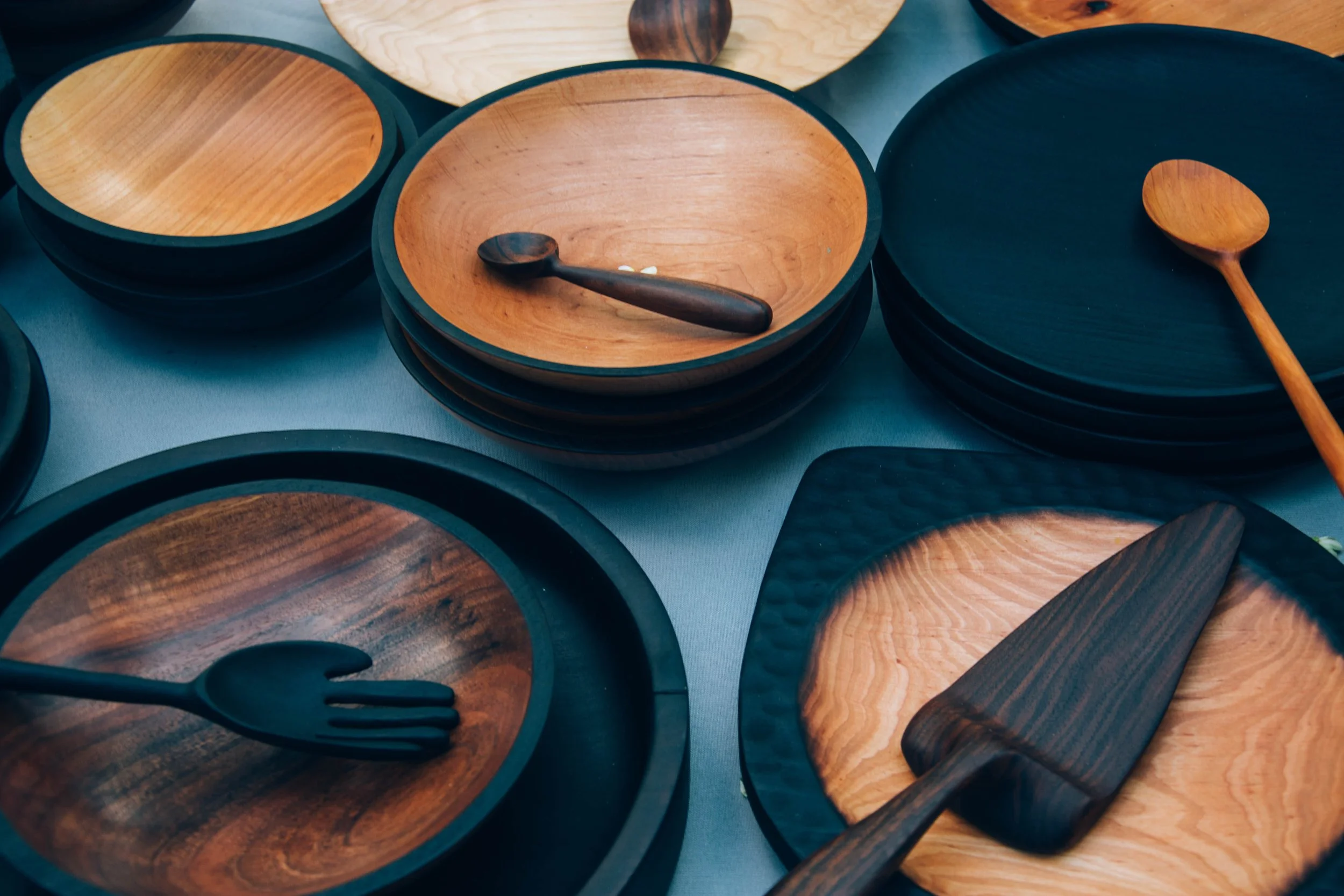 Stacks of wooden bowls, plates, and cutting boards with utensils on display.