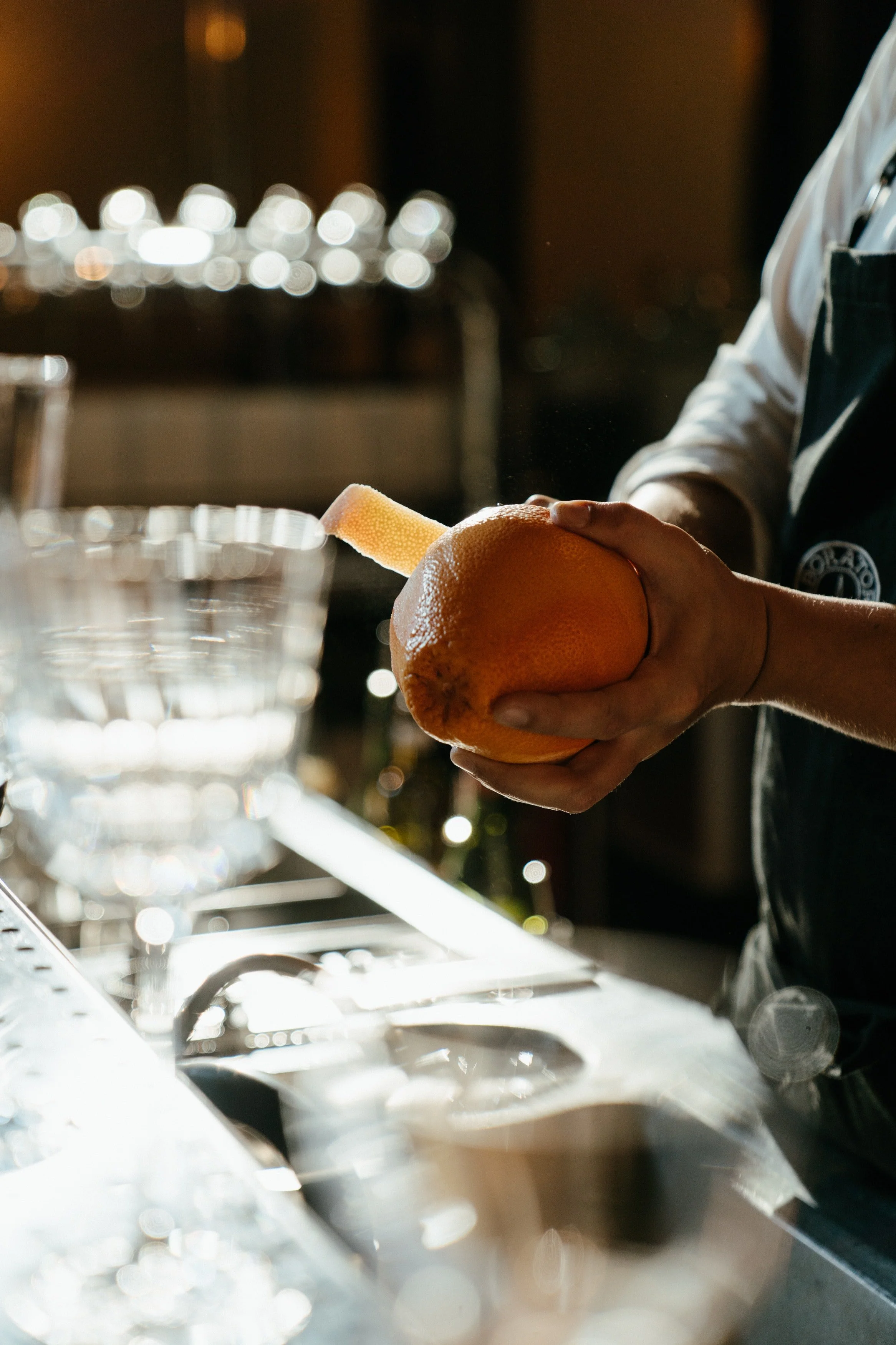 A person holding an orange and peeling it with a citrus peeler in a dimly lit setting.