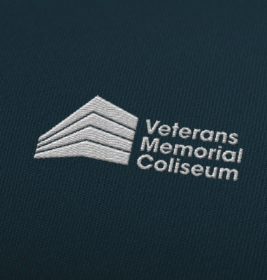 Embossed logo of Veterans Memorial Coliseum showing a stylized building and text on a dark fabric background.