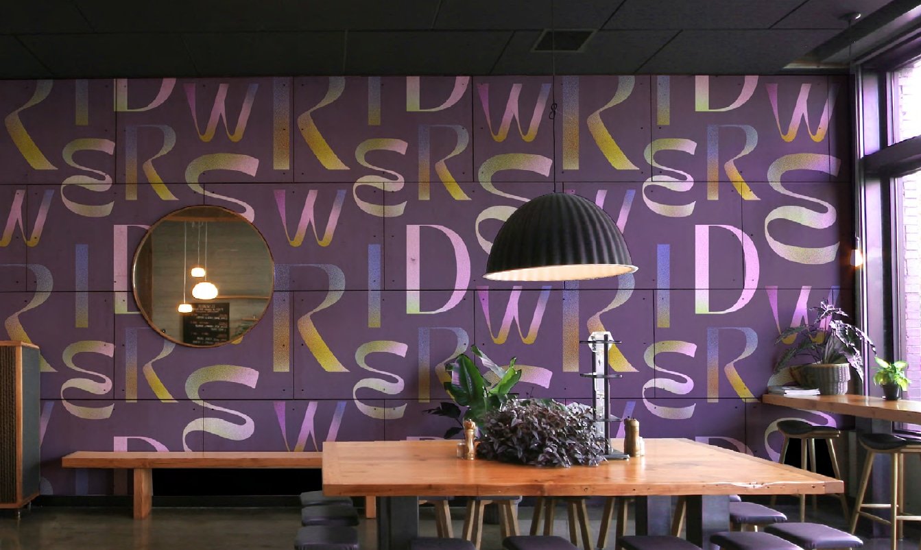 Interior of Wired cafe and restaurant showing the logo design with a purple patterned wall, a round mirror, a wooden table with chairs, and hanging pendant lighting, near a window with potted plants.