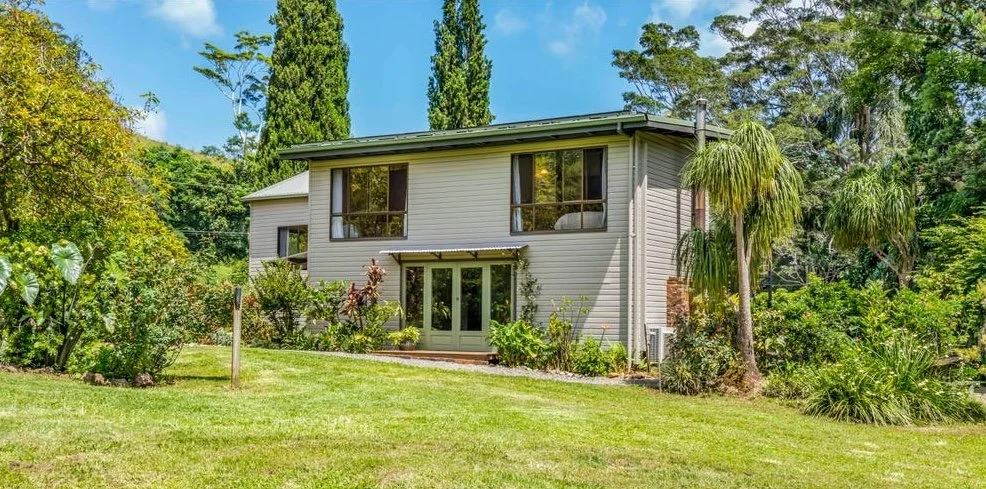 Two-story house at Rise Temple Retreat with grey siding, surrounded by lush greenery and tall trees.