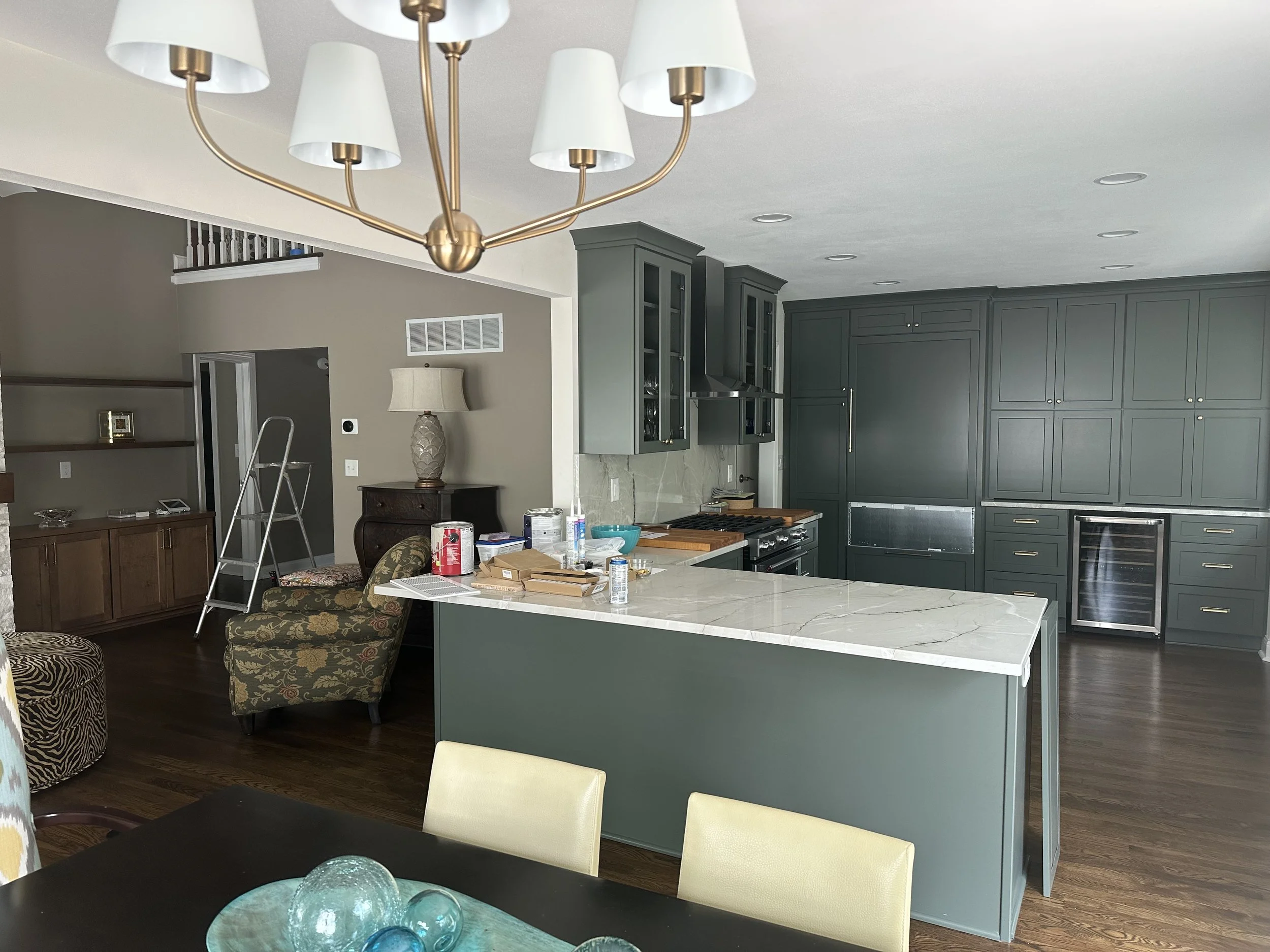 Kitchen with dark gray cabinets, white marble island, pendant lights, and cluttered countertop.