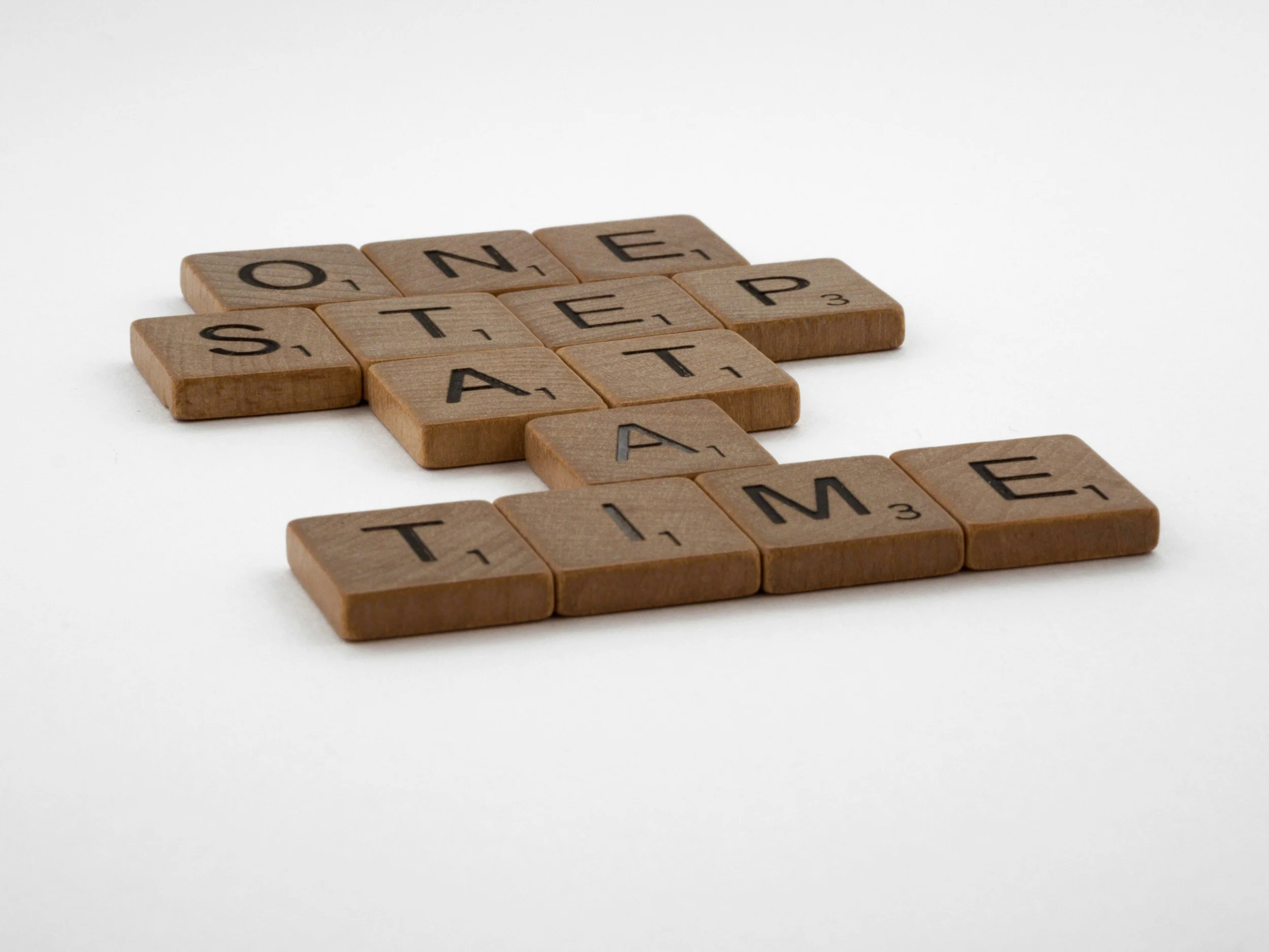 "one step at a time" spelled out in scrabble tiles