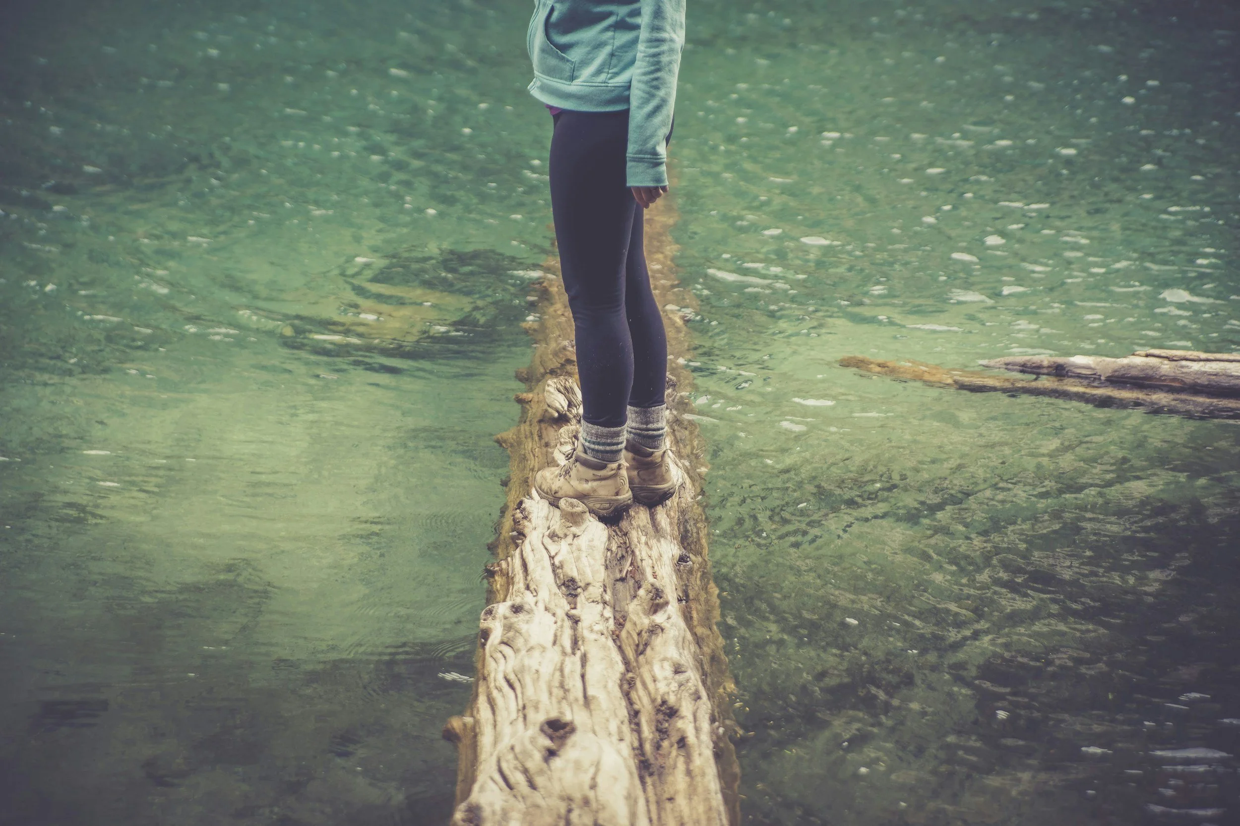 person out in the running river, standing on a big fallen tree