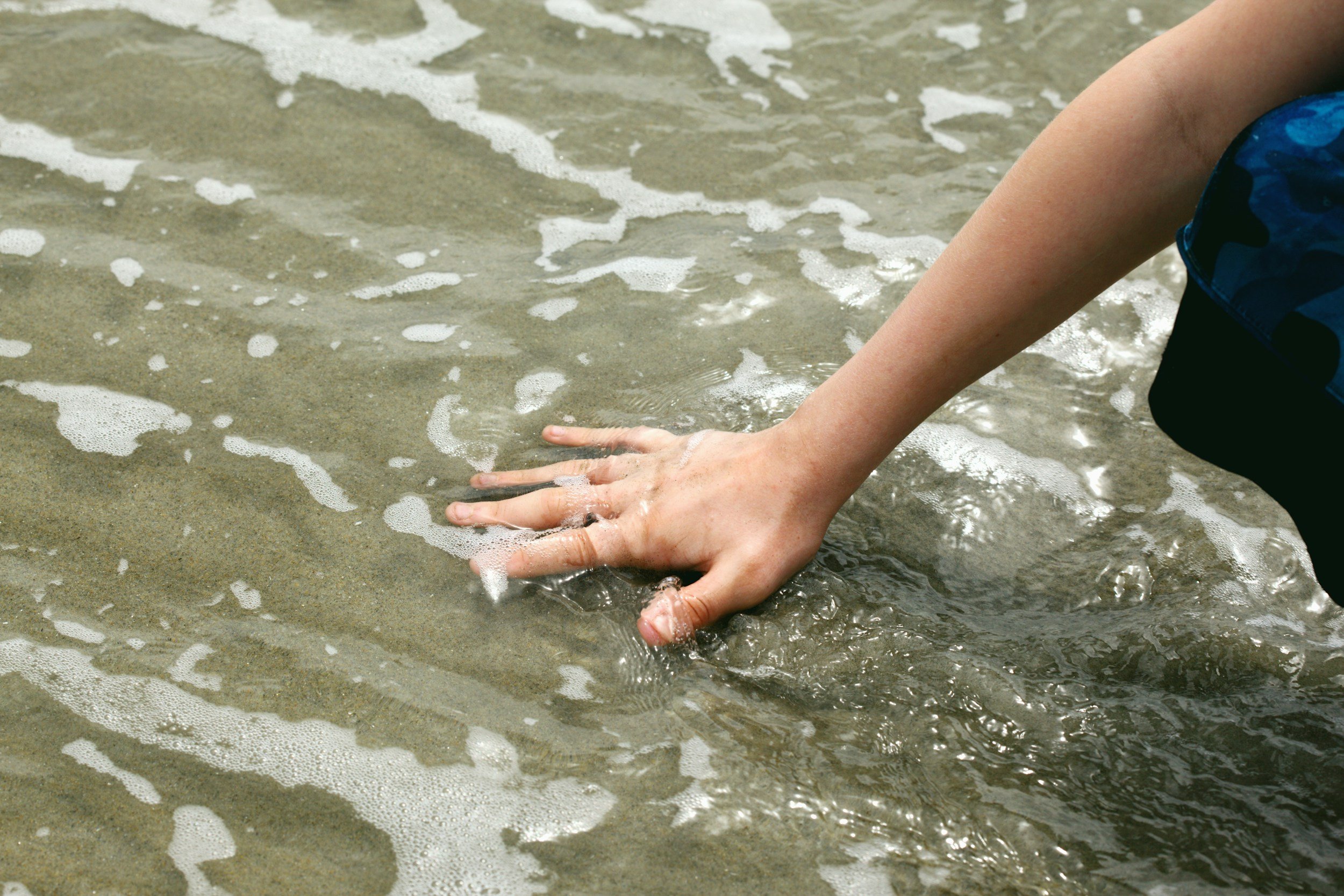hand in ocean water, touching the sand
