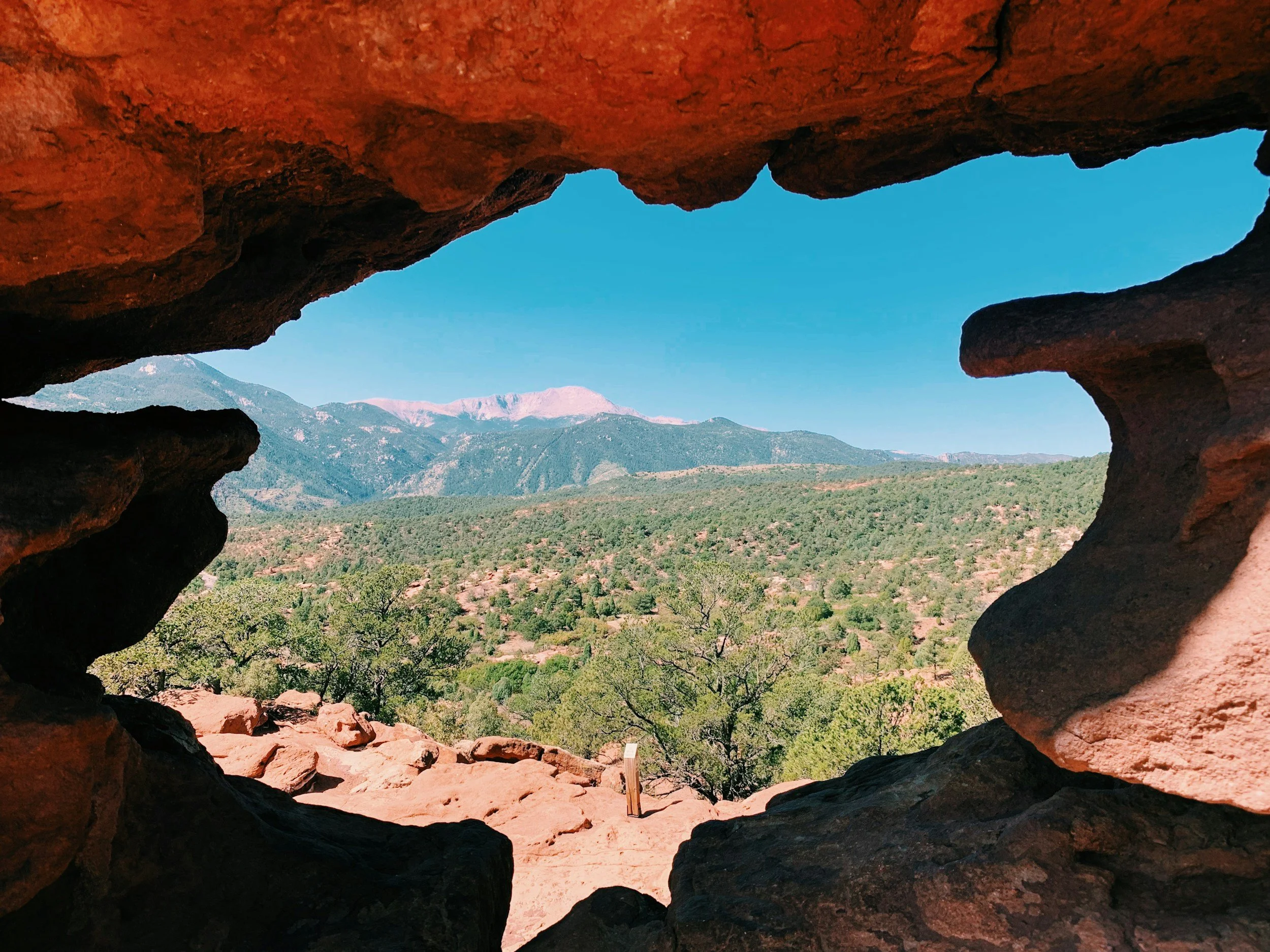 View of mountains and sky seen through a rock formation with a hole in the center in the Garden of the Gods, Colorado