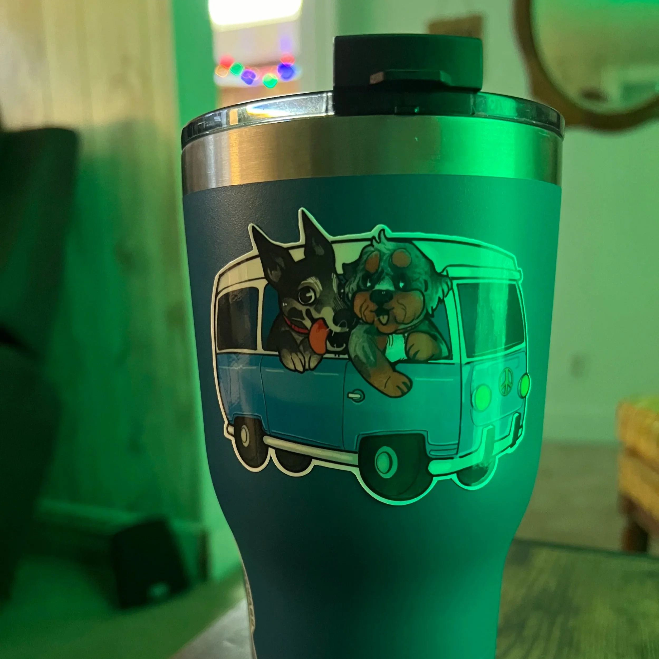 A travel tumbler with a decal of a cute cartoon dog and cat sticking out of a blue van.