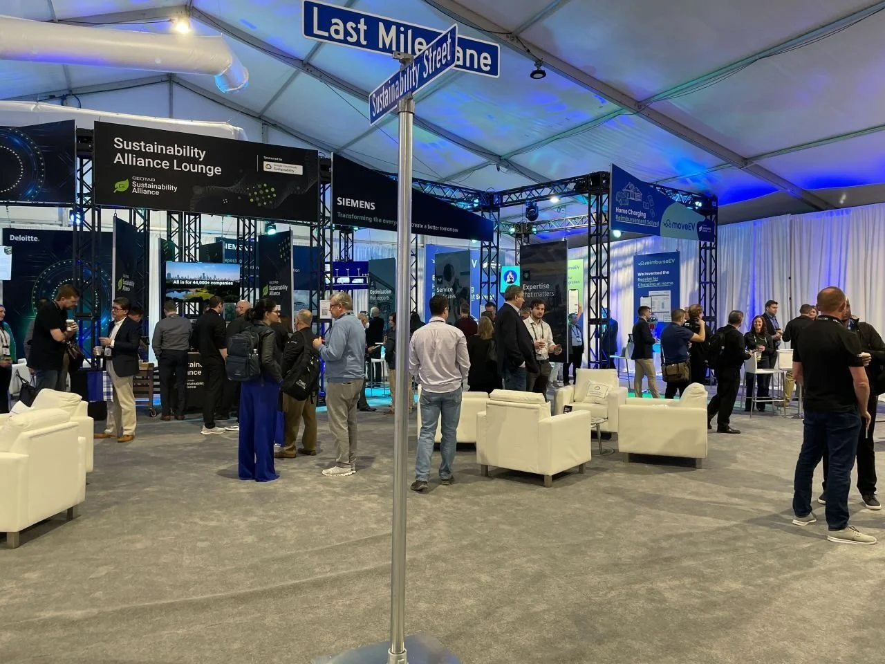 ttendees and exhibitors networking in the Sustainability Alliance Lounge at Geotab Connect 2024, featuring mock street signs for 'Sustainability Street' and 'Last Mile Lane'.