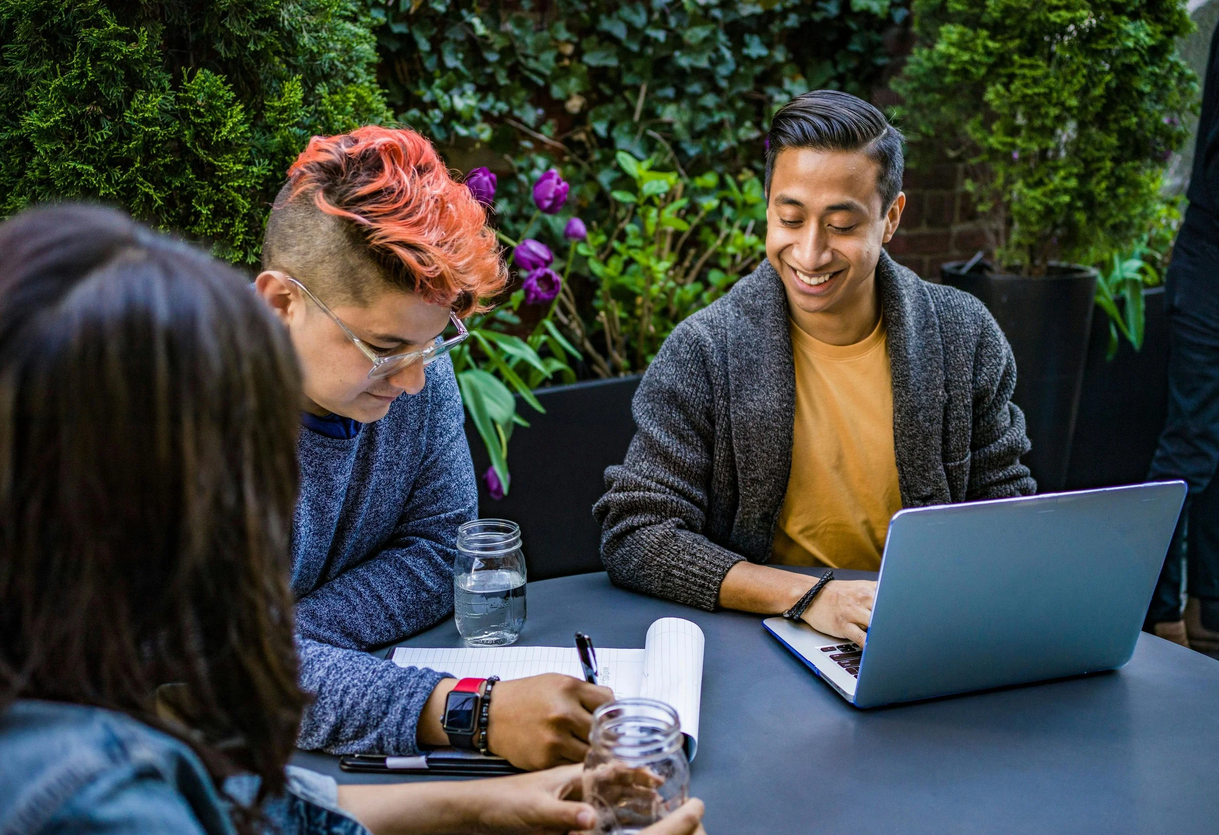 Three people one with pink-colored hair gather around a table together therapy in Chicago