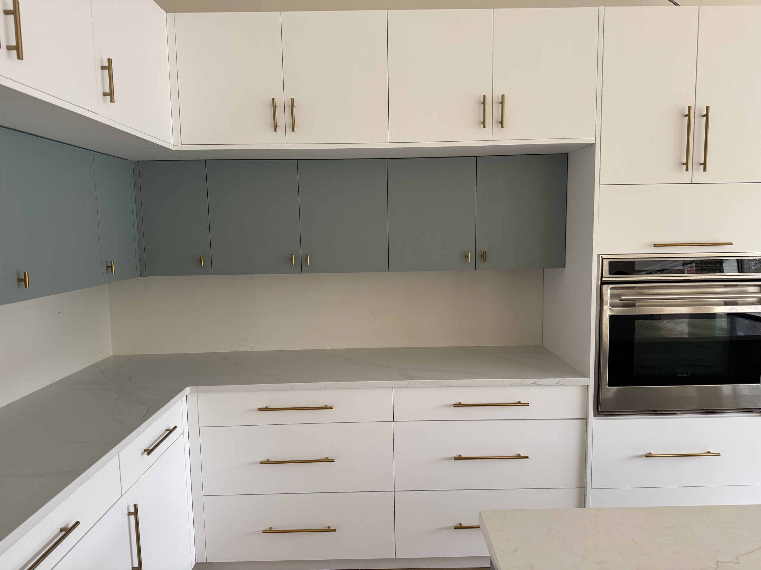 Modern kitchen with white and gray cabinets, gold handles, marble countertops, and a built-in stainless steel oven.