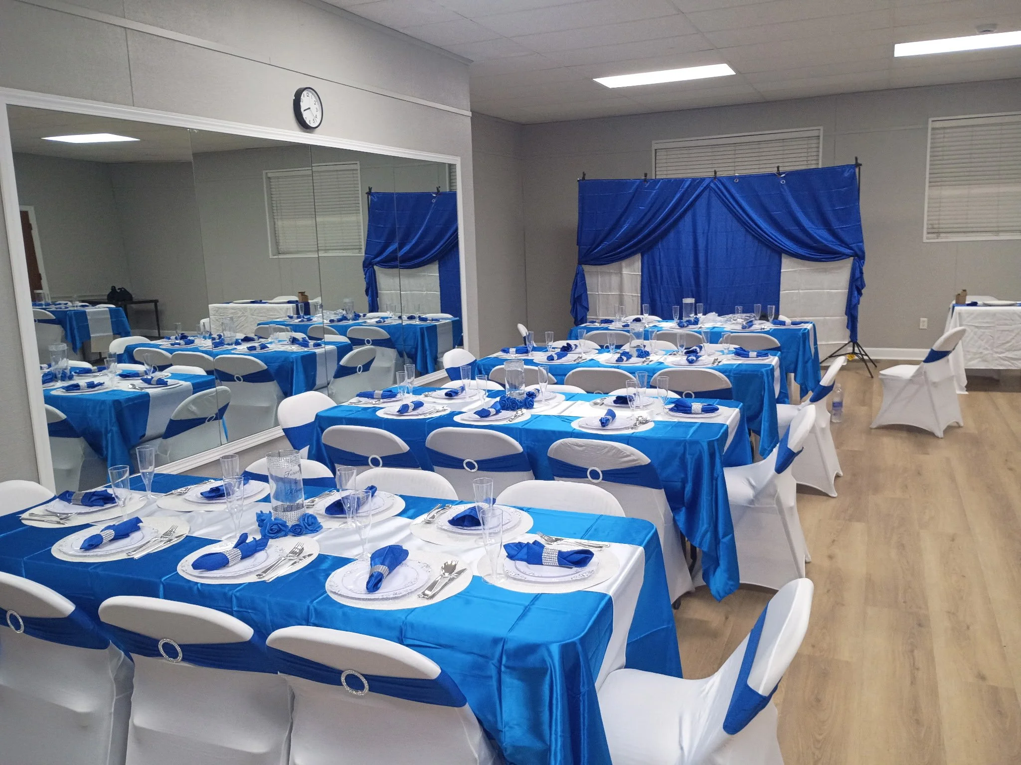 A banquet hall decorated for an event with blue and white table settings, tied with blue ribbons, and a stage with blue curtains.