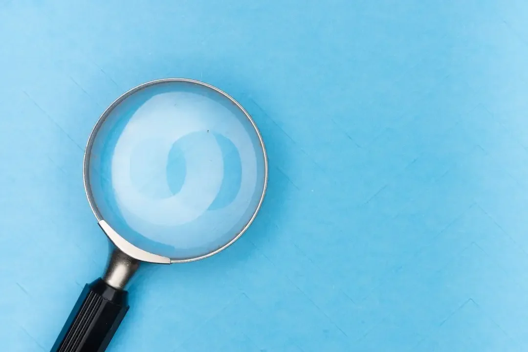 A magnifying glass with water inside, reflecting a question mark, on a blue surface.