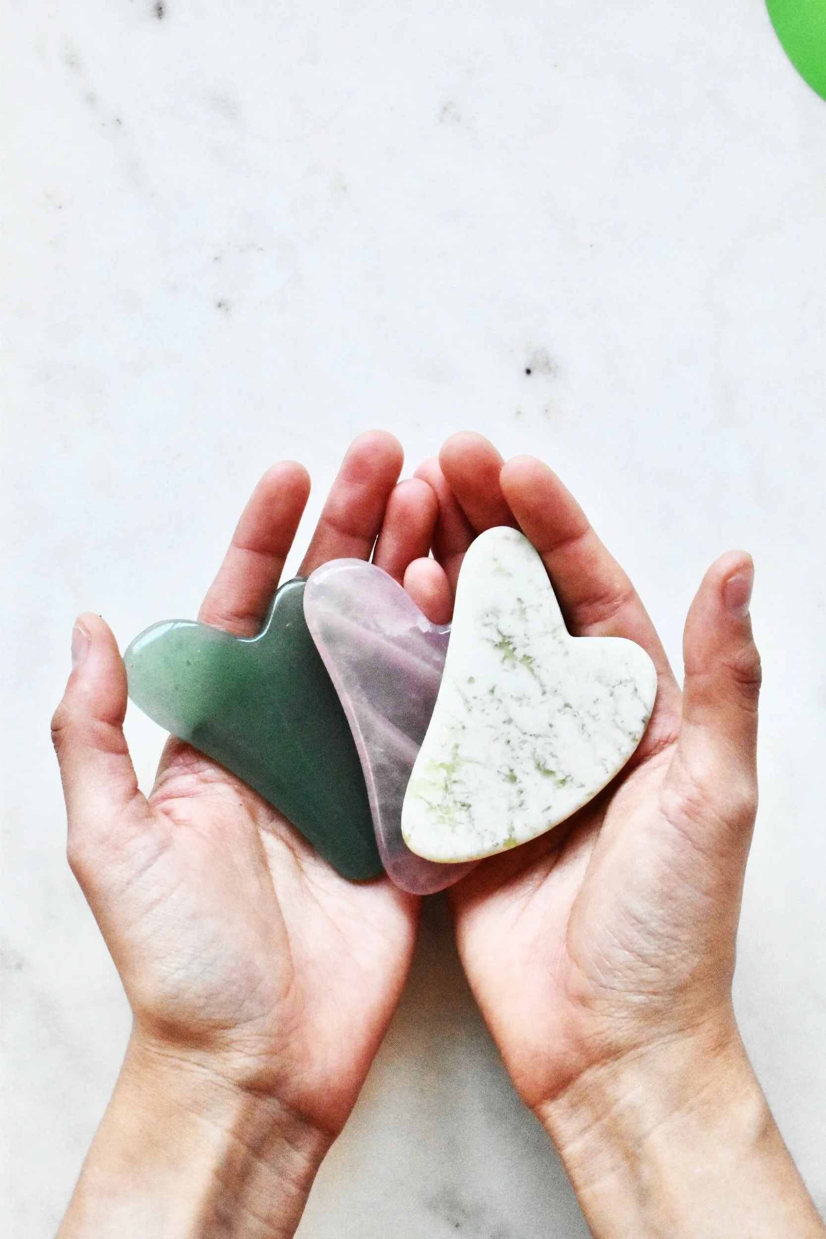 Two hands holding flat gua sha tools made of various stones.