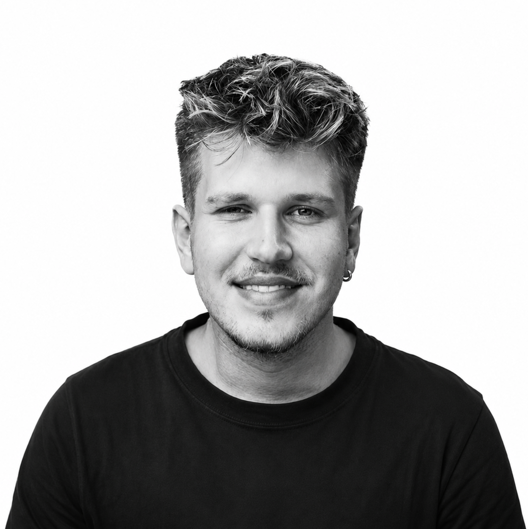 Schwarz-weiße Nahaufnahme eines jungen Mannes mit kurzen, dunkel, gewellten Haaren, einem kleinen Ohrring im linken Ohr, lächelnd, gegen einen weißen Hintergrund.