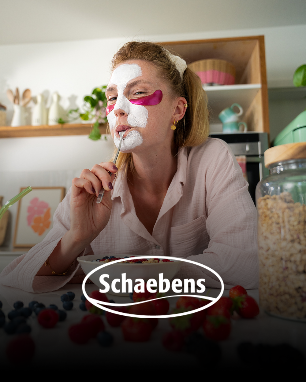 Frau mit Gesichtsmasken und Gesichtsbart beim Frühstück mit Beeren, umgeben von Müsli und Frühstückszubehör in einer modernen Küche.