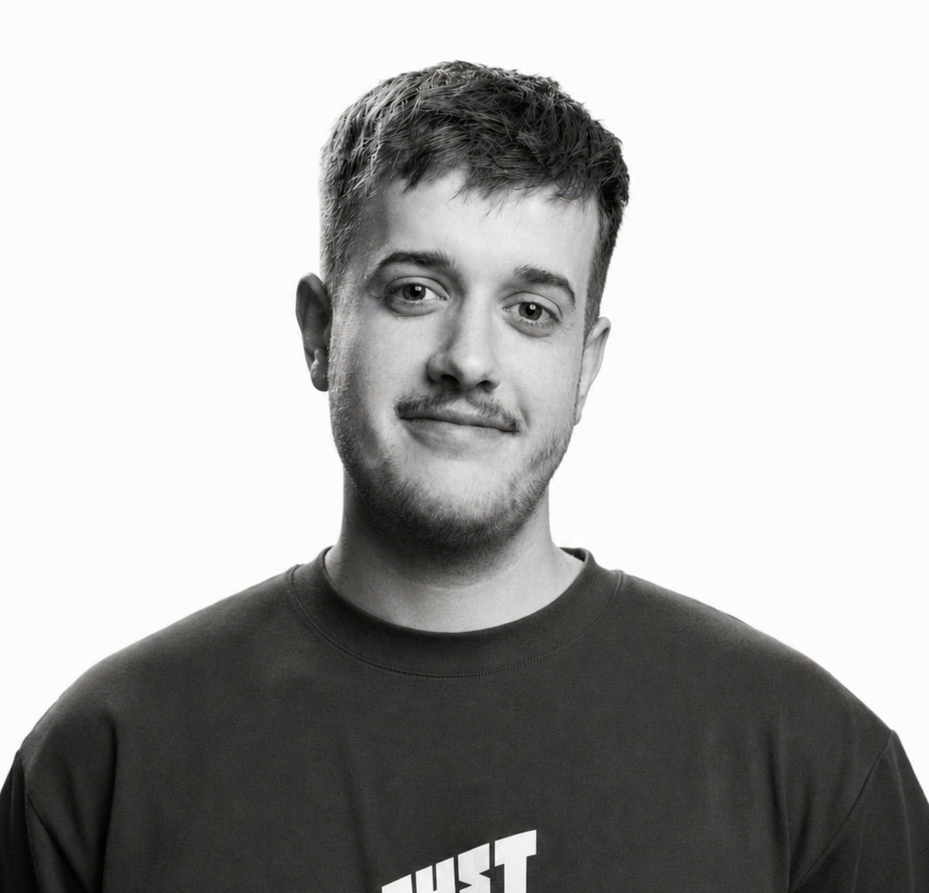 Schwarz-weißes Porträt eines jungen Mannes mit kurzen, gewellten Haaren, leichtem Bart, in einem schwarzen T-Shirt mit weißem Nike-Logo, vor hellem Hintergrund.